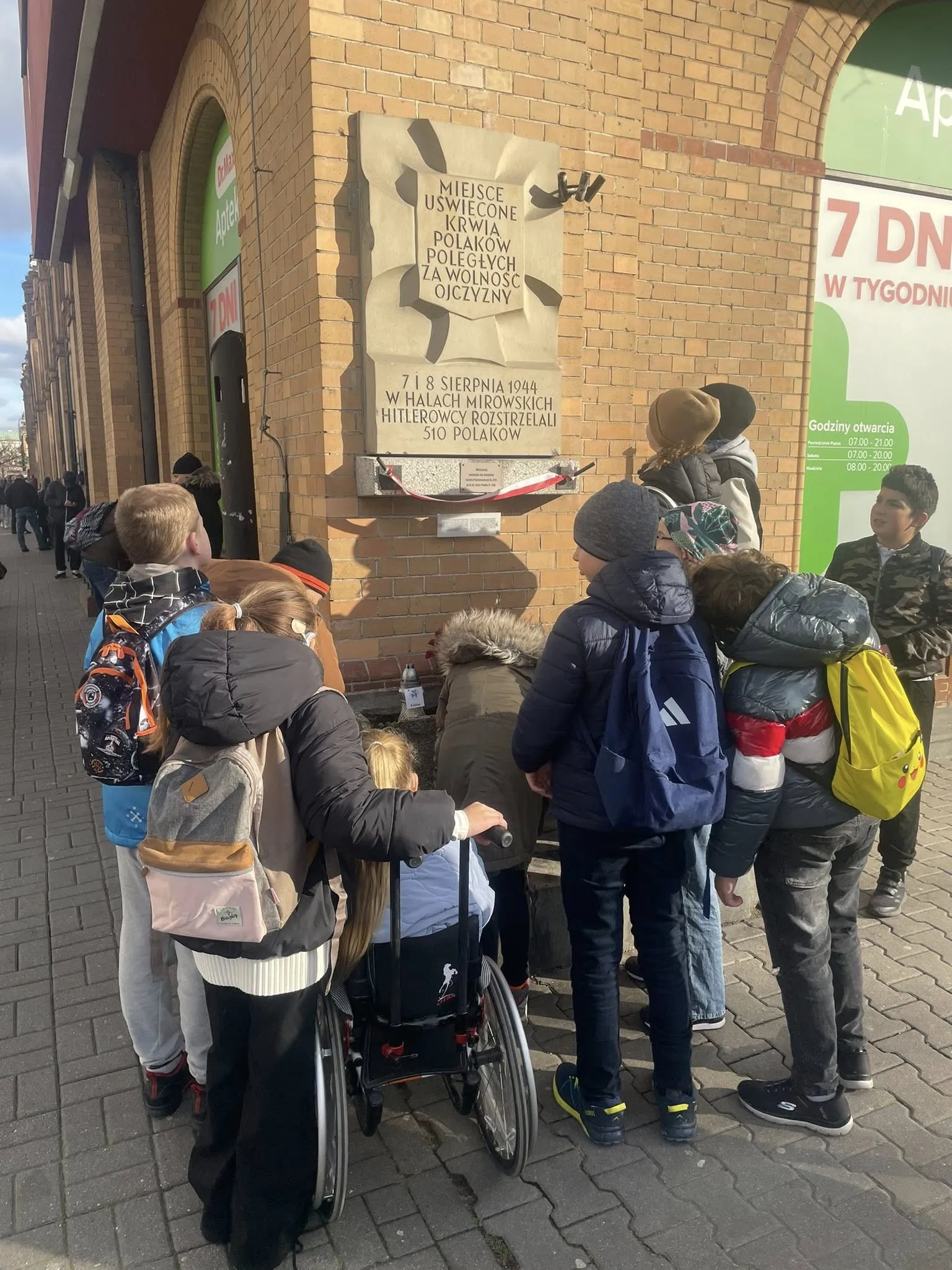 Uczniowie pod tablicą upamiętniającą egzekucję Polaków w Halach Mirowskich
