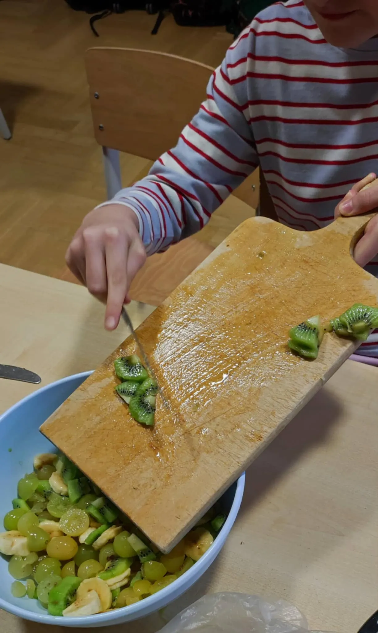 Uczeń zsuwający z deski pokrojone owoce do miski