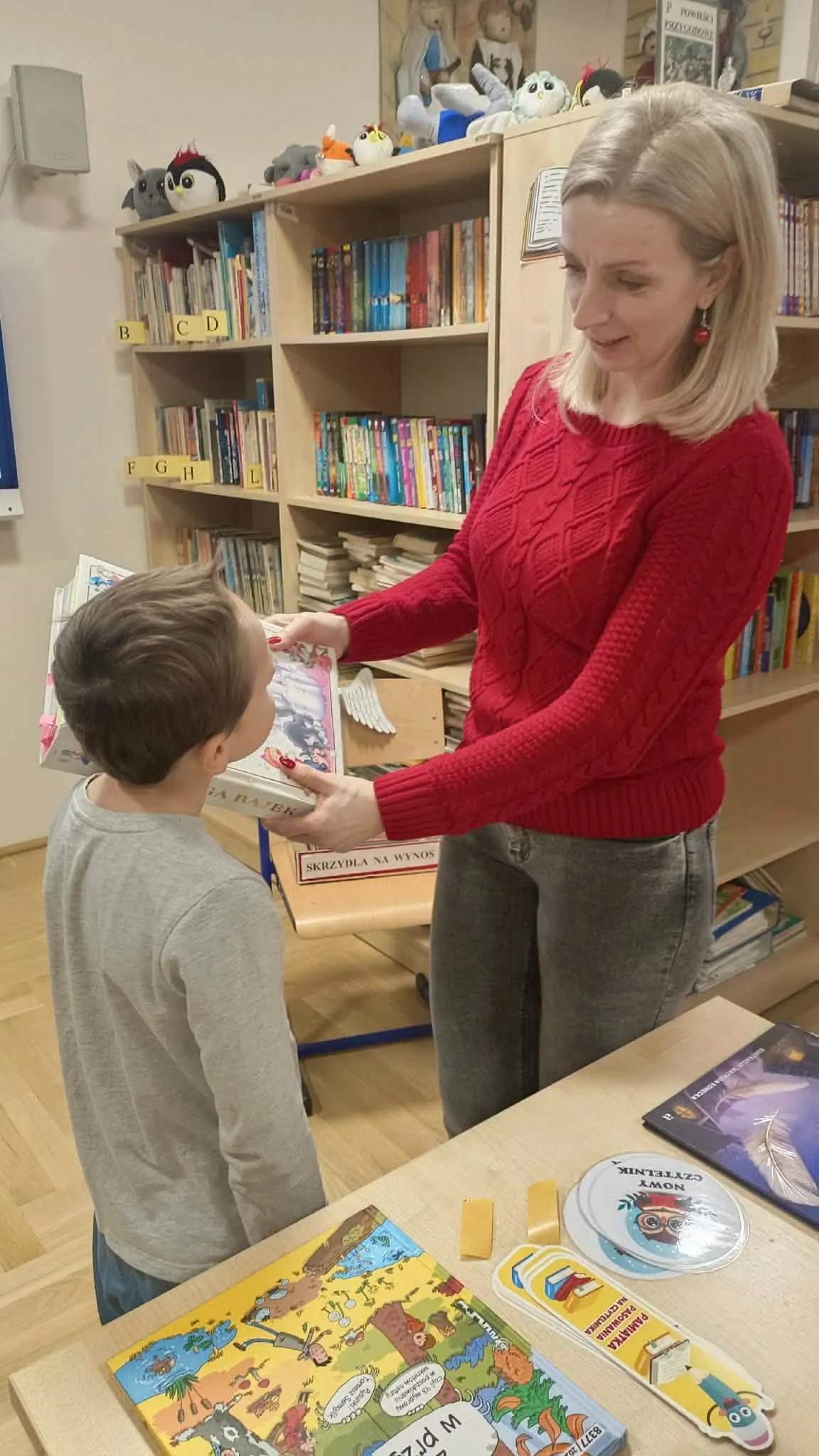 Nauczycielka pasuje dziecko książką na czytelnika.