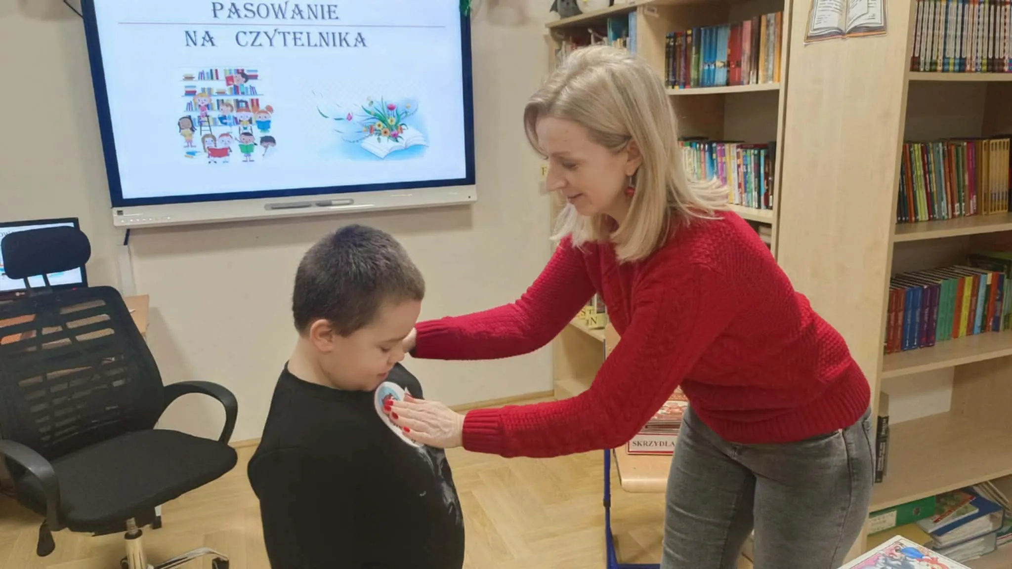 Nauczycielka przypina odznakę uczniowi.