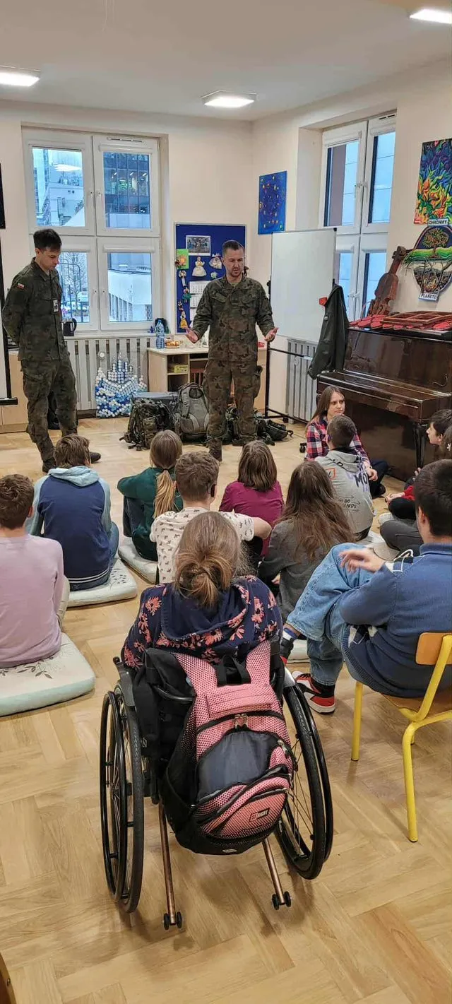 Uczniowie siedzący na podłodze w sali podczas zajęć tematycznych pod kierunkiem  żołnierzy