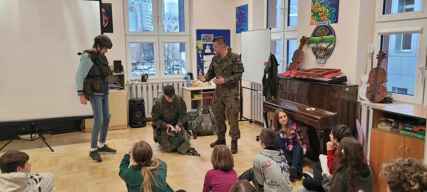 Uczeń z pomocą żołnierzy przymierza wojskowy strój specjalistyczny