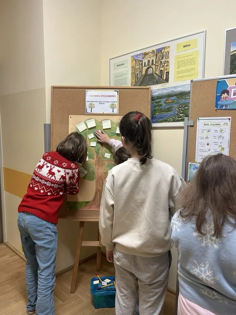 Uczniowie odrywający kartki z tablicy życzliwośći 