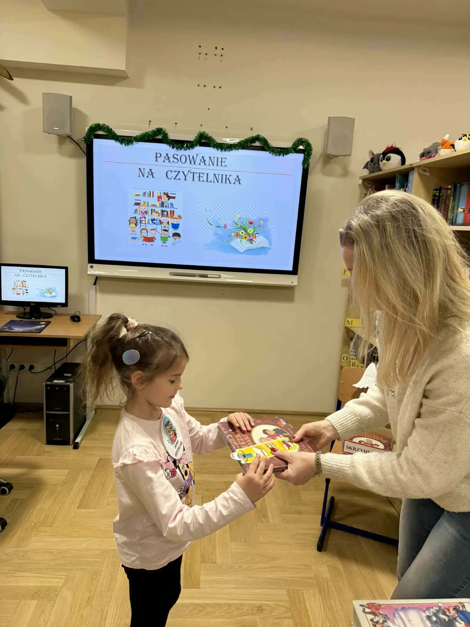 Uczennica odbiera książkę od nauczycielki.