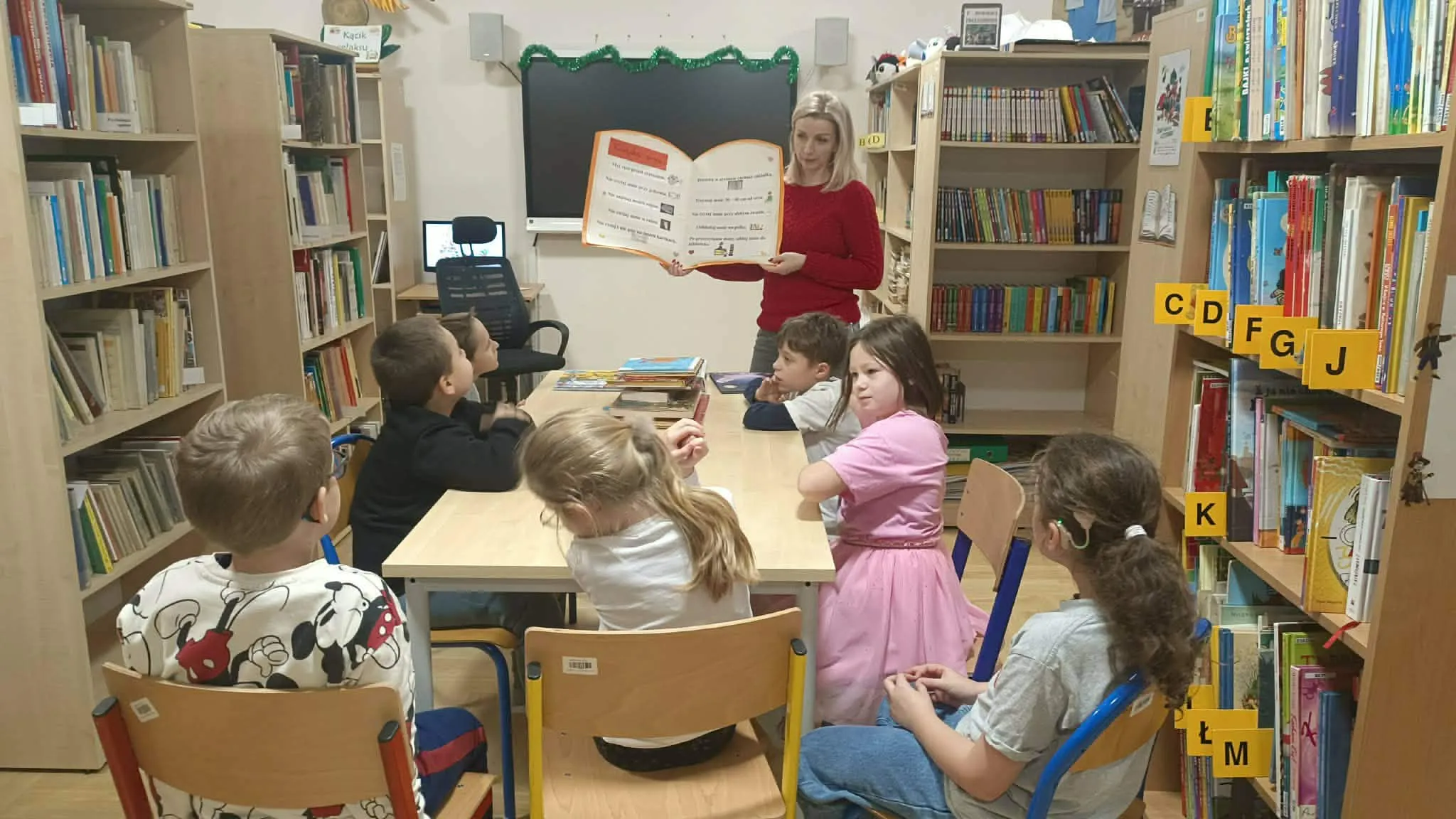 Dzieci słuchają czytania w bibliotece.