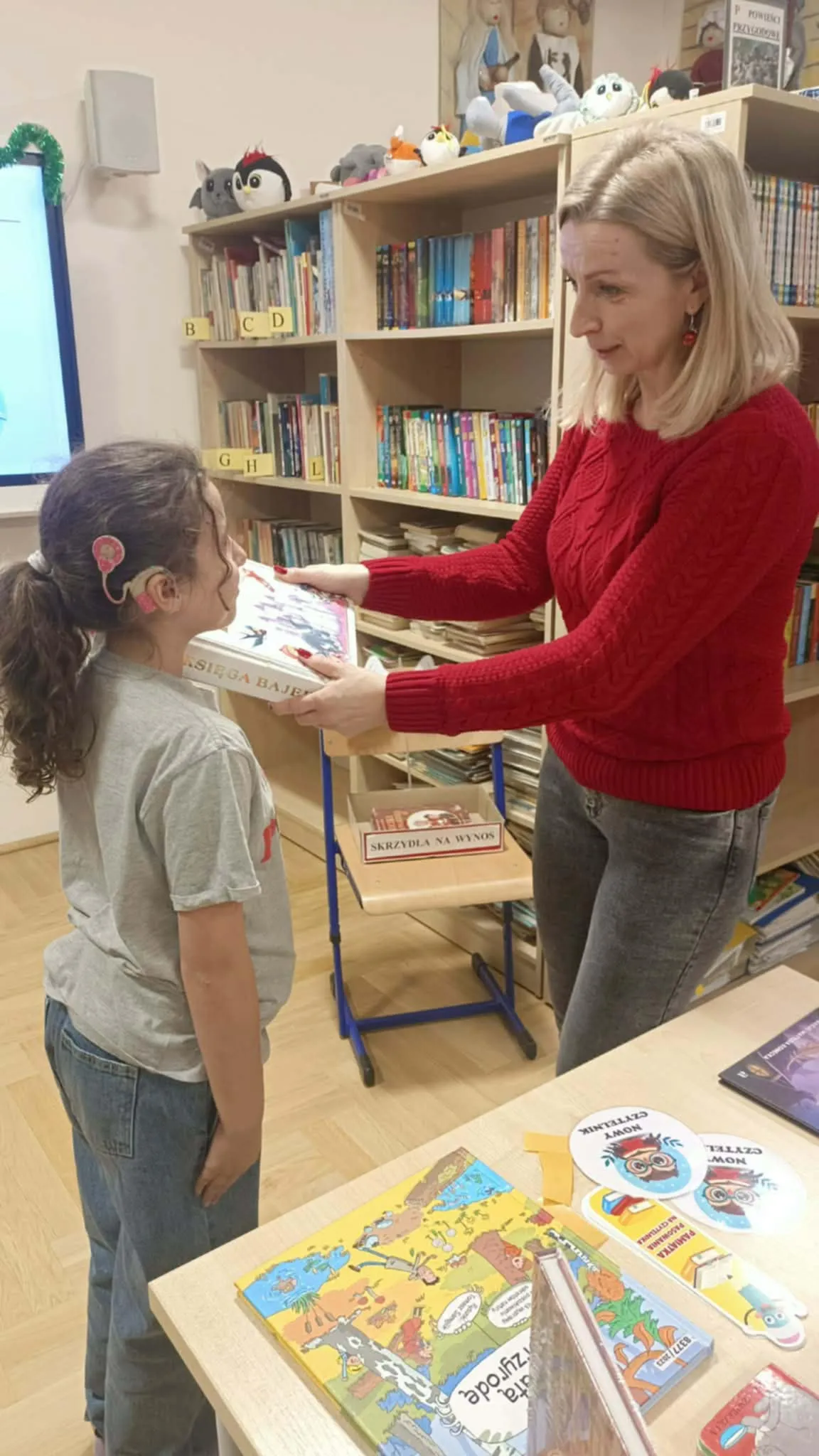 Nauczycielka pasuje uczennicę książką na czytelnika.