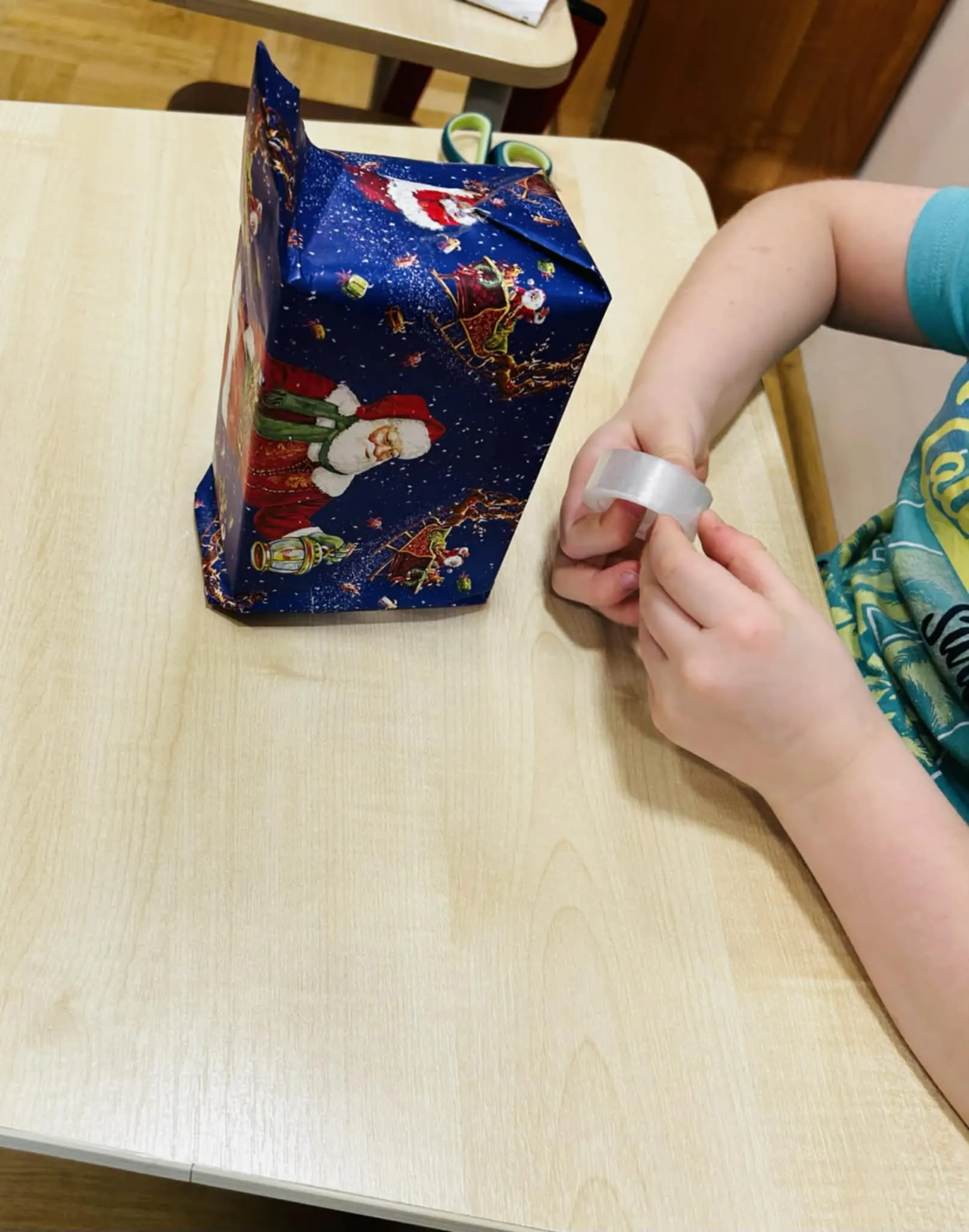 Zapakowany prezent i ręce trzymające taśmę klejącą.