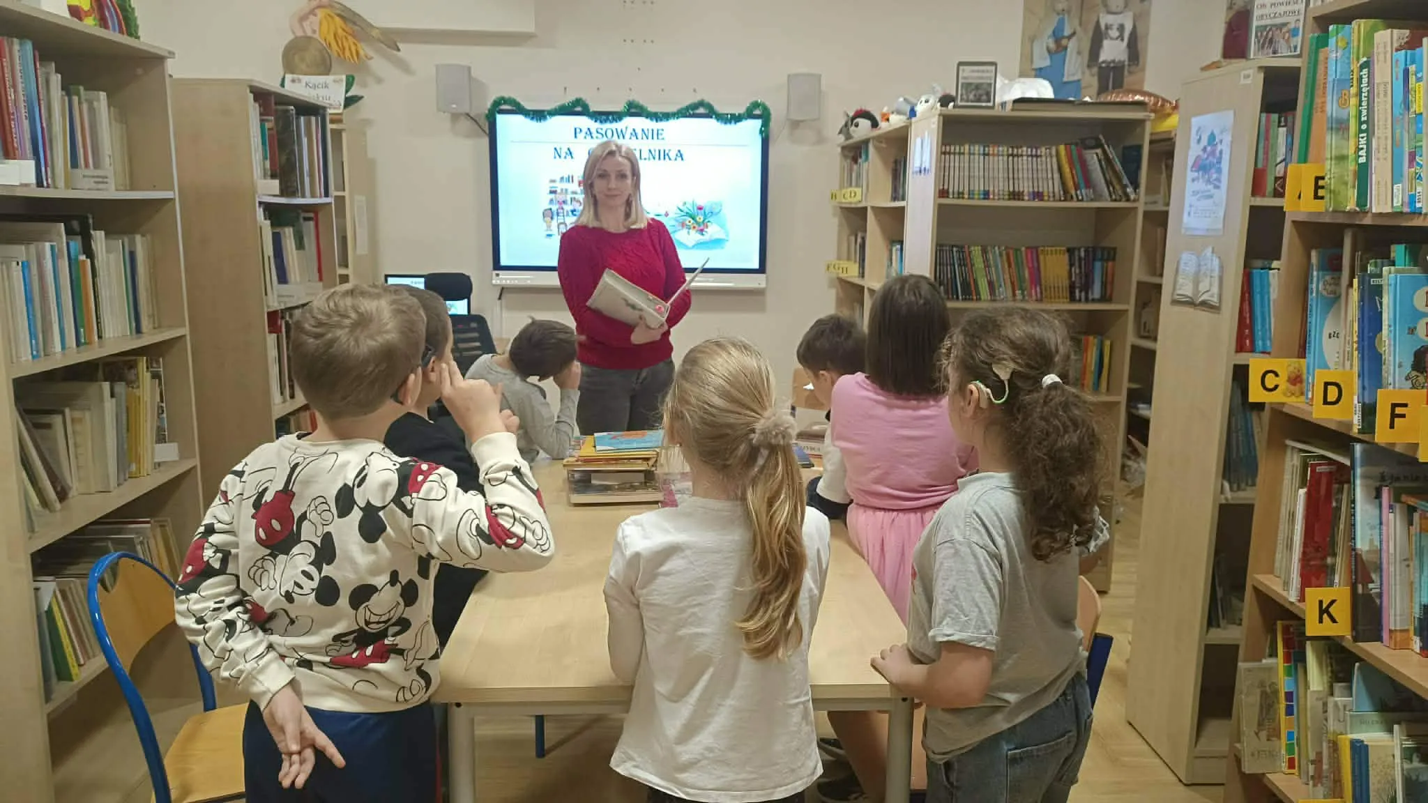 Nauczycielka stoi przed dziećmi w bibliotece.
