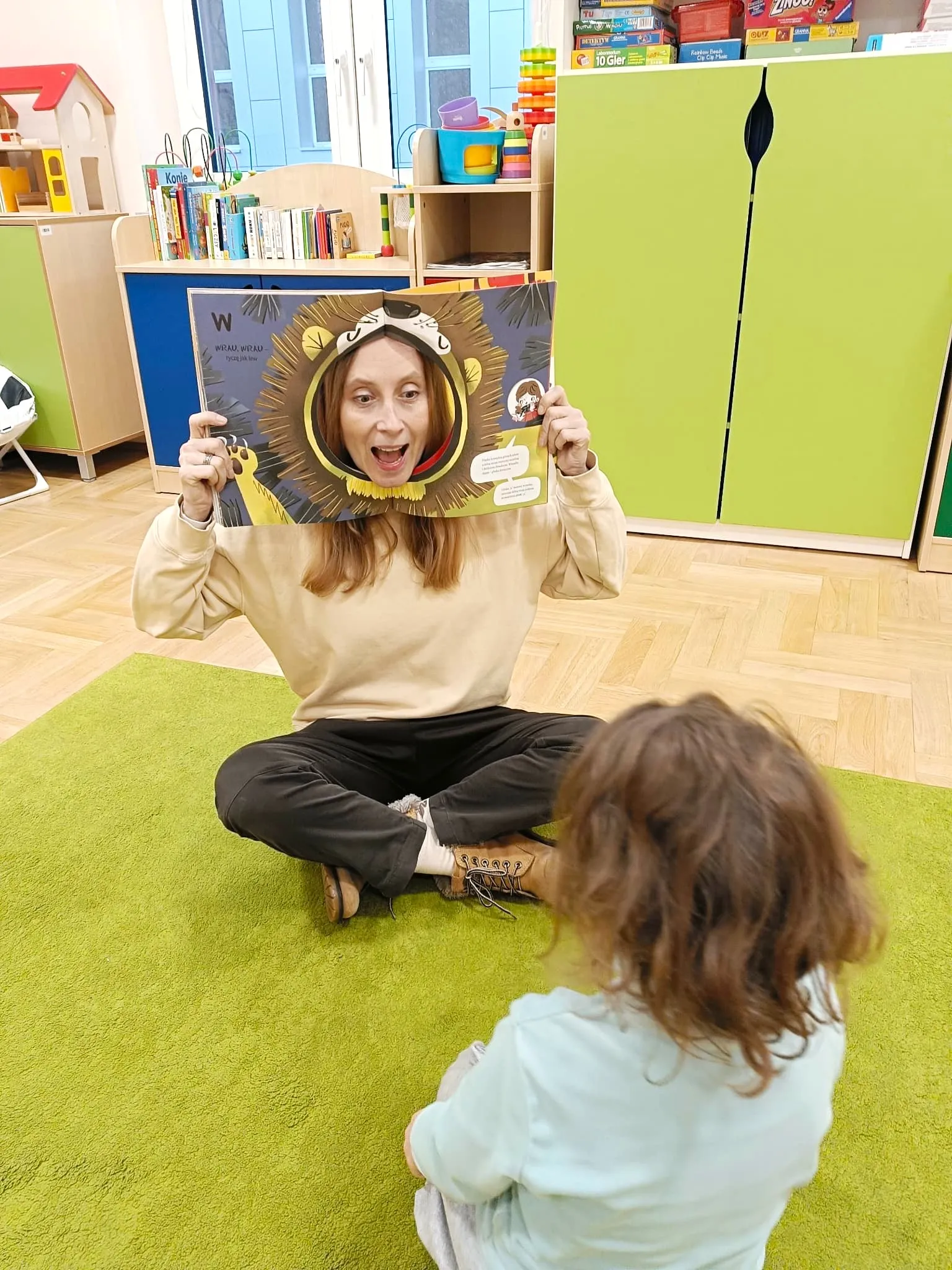 Dziewczynka siedząca na dywanie na przeciwko terapeuty podczas zajęć logopedycznych