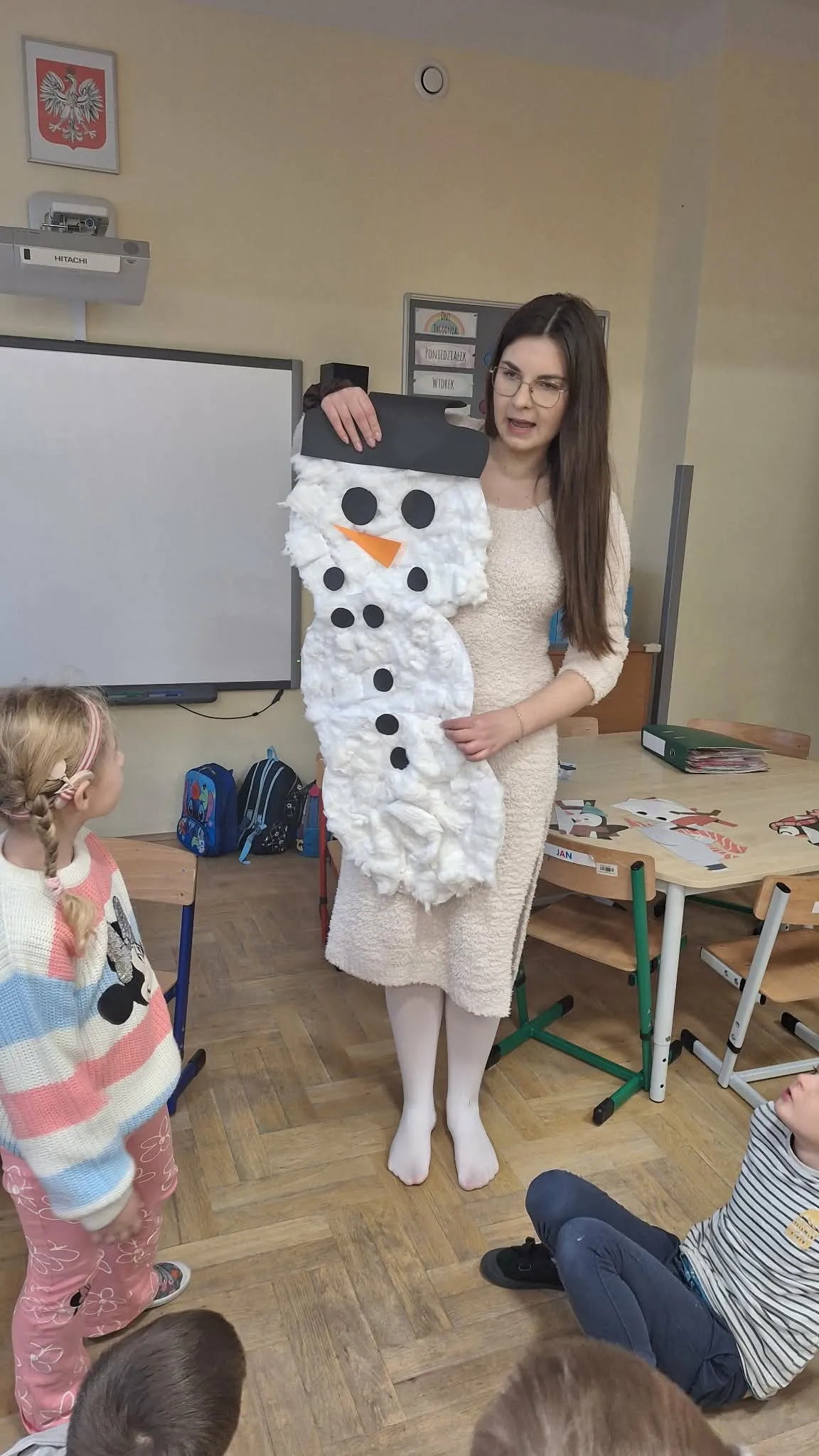Nauczycielka prezentuje dzieciom dużą pracę plastyczną przedstawiającą bałwana wykonanego z waty.