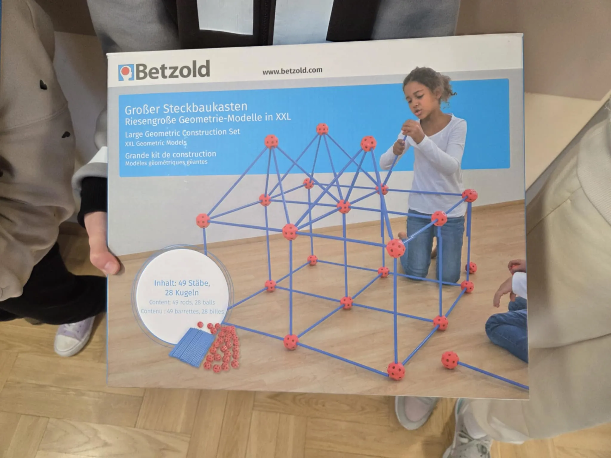 Zbliżenie na opakowanie dużego zestawu konstrukcyjnego do budowania modeli geometrycznych, trzymane przez dziecko.