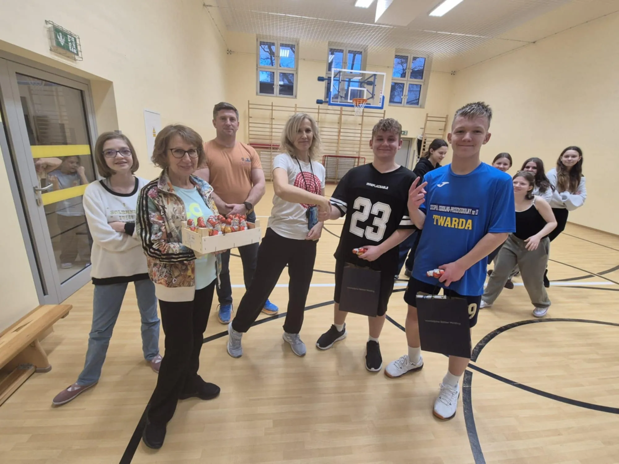 Wspólne zdjęcie po zakończeniu zawodów – uczniowie i nauczyciele w sali gimnastycznej z nagrodami i upominkami.