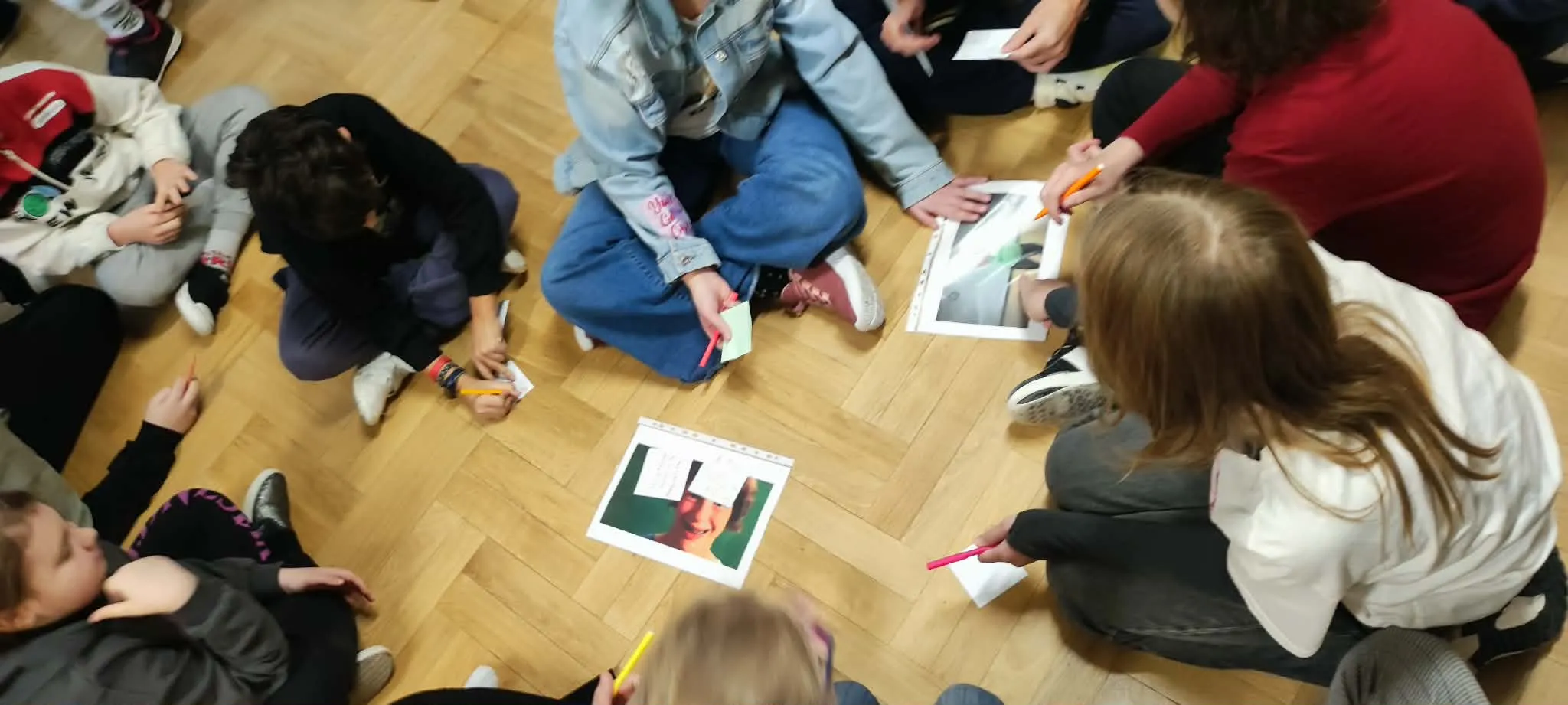 Uczniowie rozwiązujący zadanie siedząc na korytarzu szkolnym