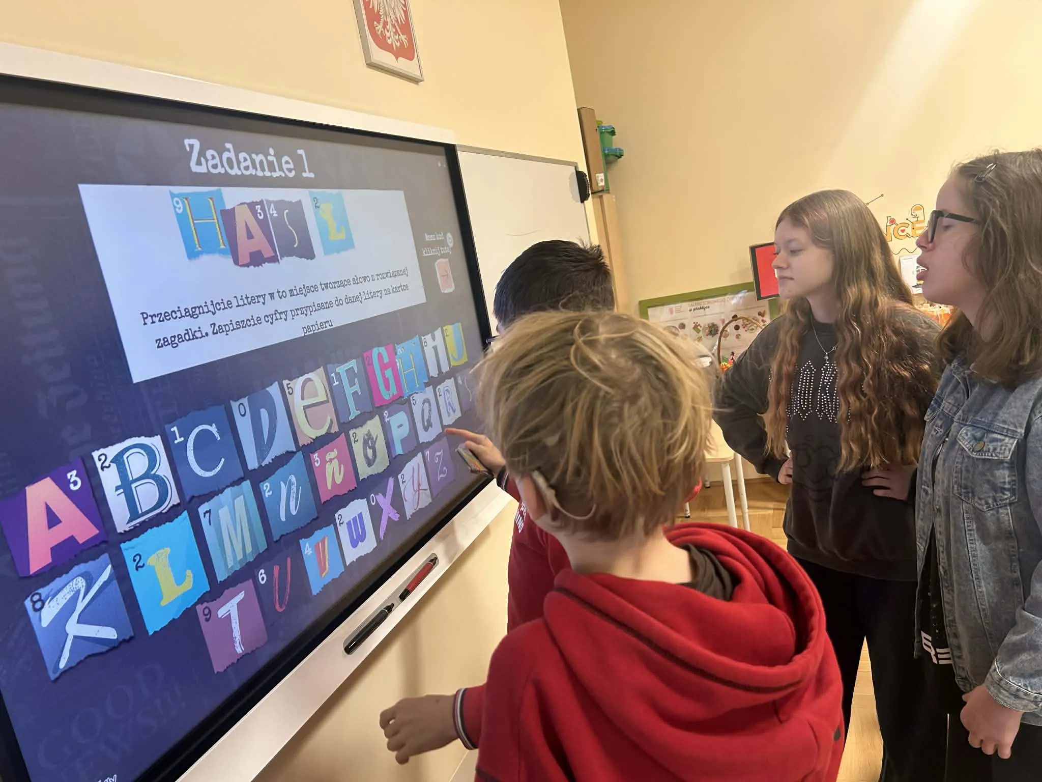 uczniowie stoją przed tablicą interaktywną i rozwiązują zadania