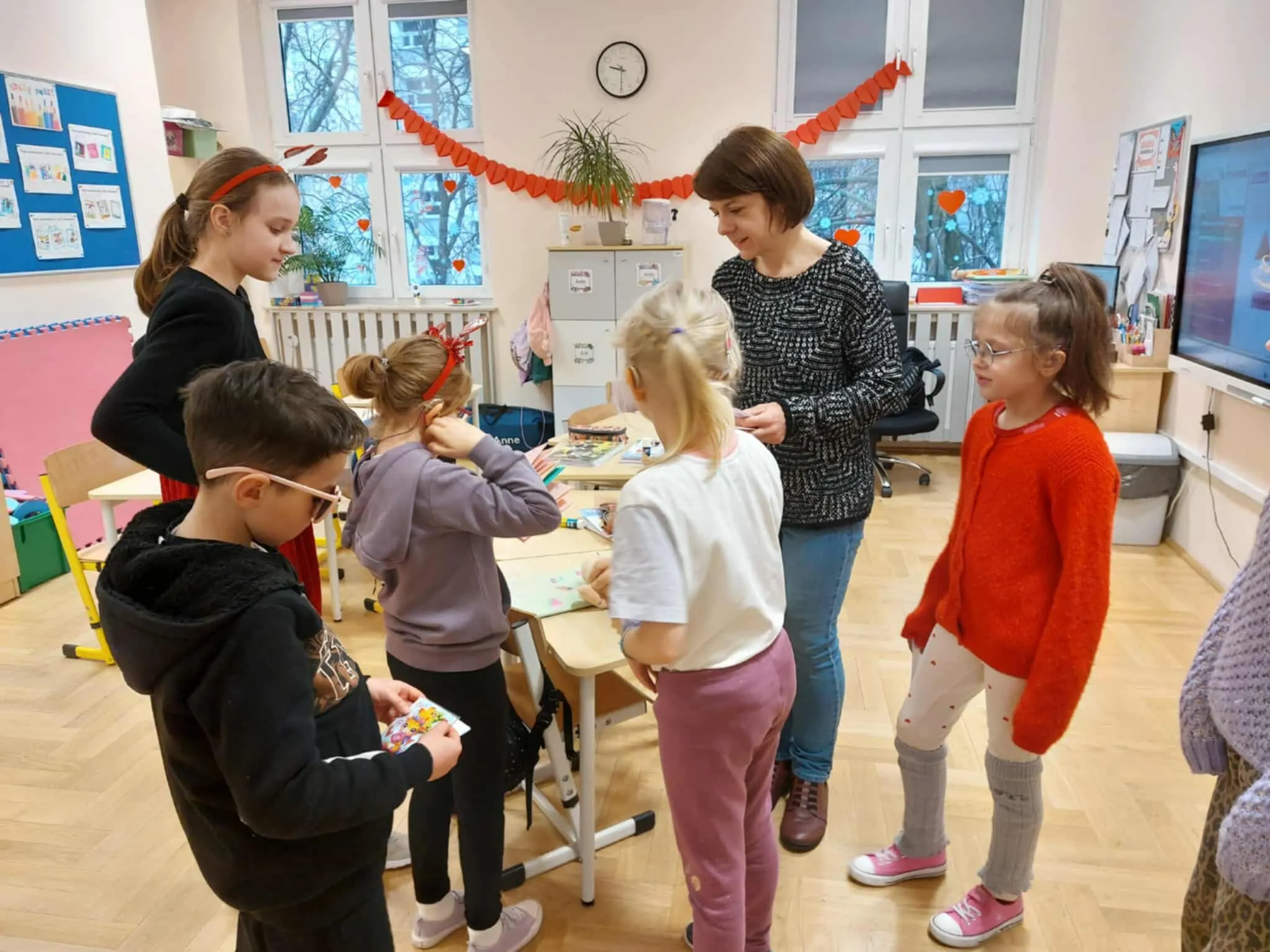 Dzieci gromadzą się wokół nauczycielki, trzymając walentynkowe kartki i rozmawiając o otrzymanych życzeniach.