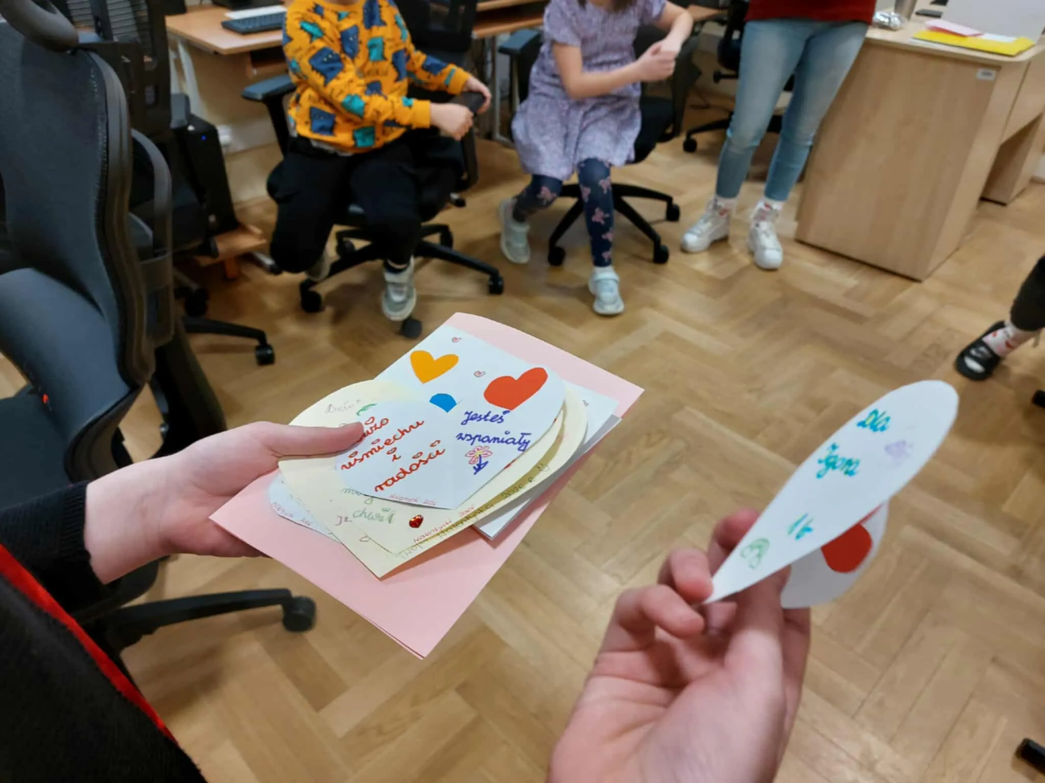 Zbliżenie na ręce uczniów trzymających kolorowe walentynkowe kartki z sercami i miłymi wiadomościami.