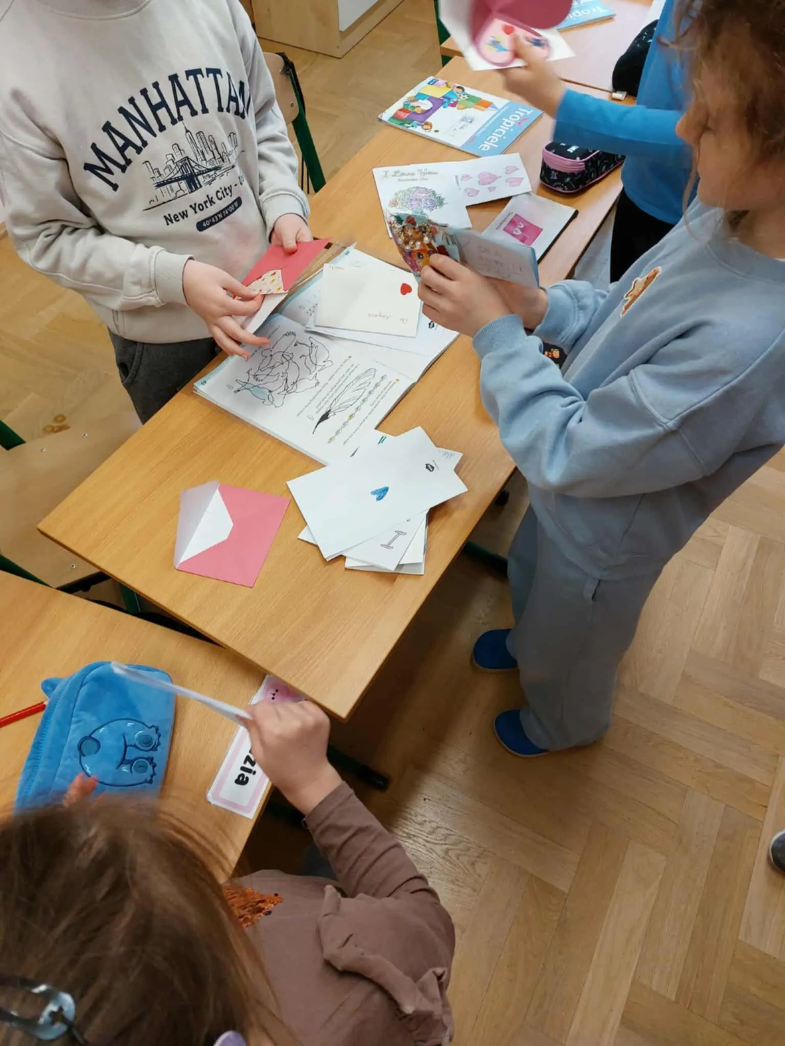Dzieci stoją przy ławkach i wspólnie oglądają oraz czytają otrzymane walentynkowe kartki i listy.