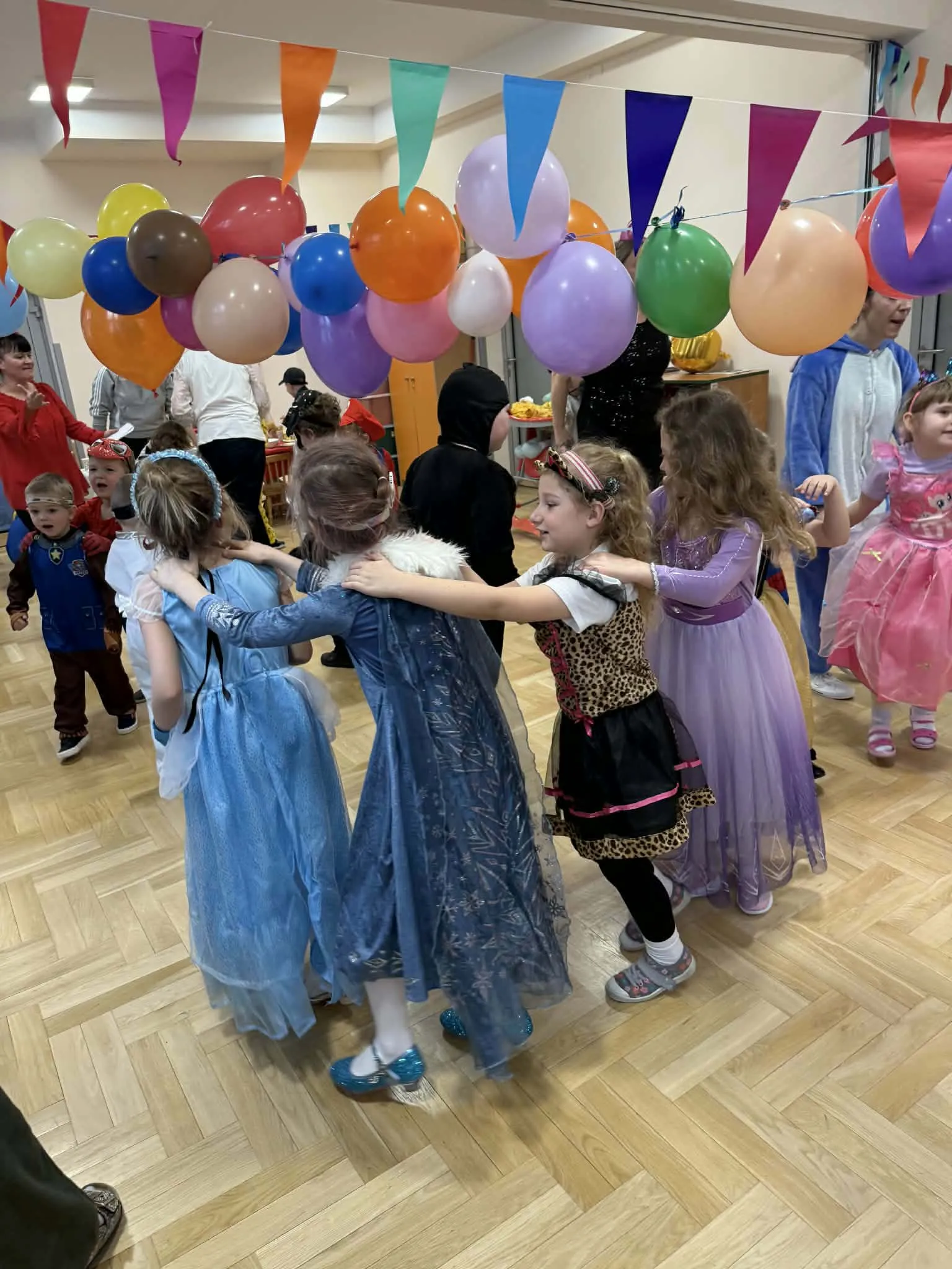 Dzieci w przebraniach tańczą w pociągu karnawałowym pod kolorowymi balonami.