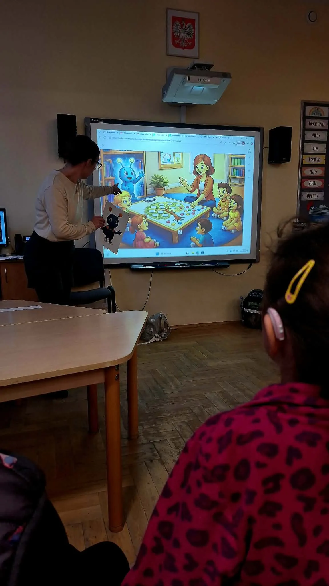 Nauczycielka wskazuje ilustrację na tablicy interaktywnej podczas zajęć z dziećmi.