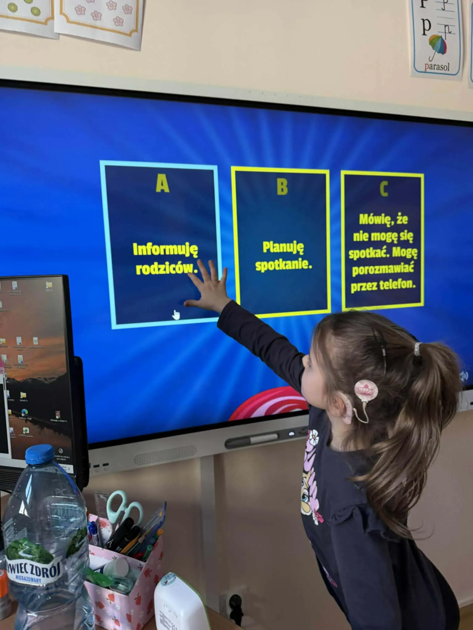 Uczennica dotyka ekranu tablicy interaktywnej, wybierając odpowiedź w ćwiczeniu o bezpiecznych zachowaniach.