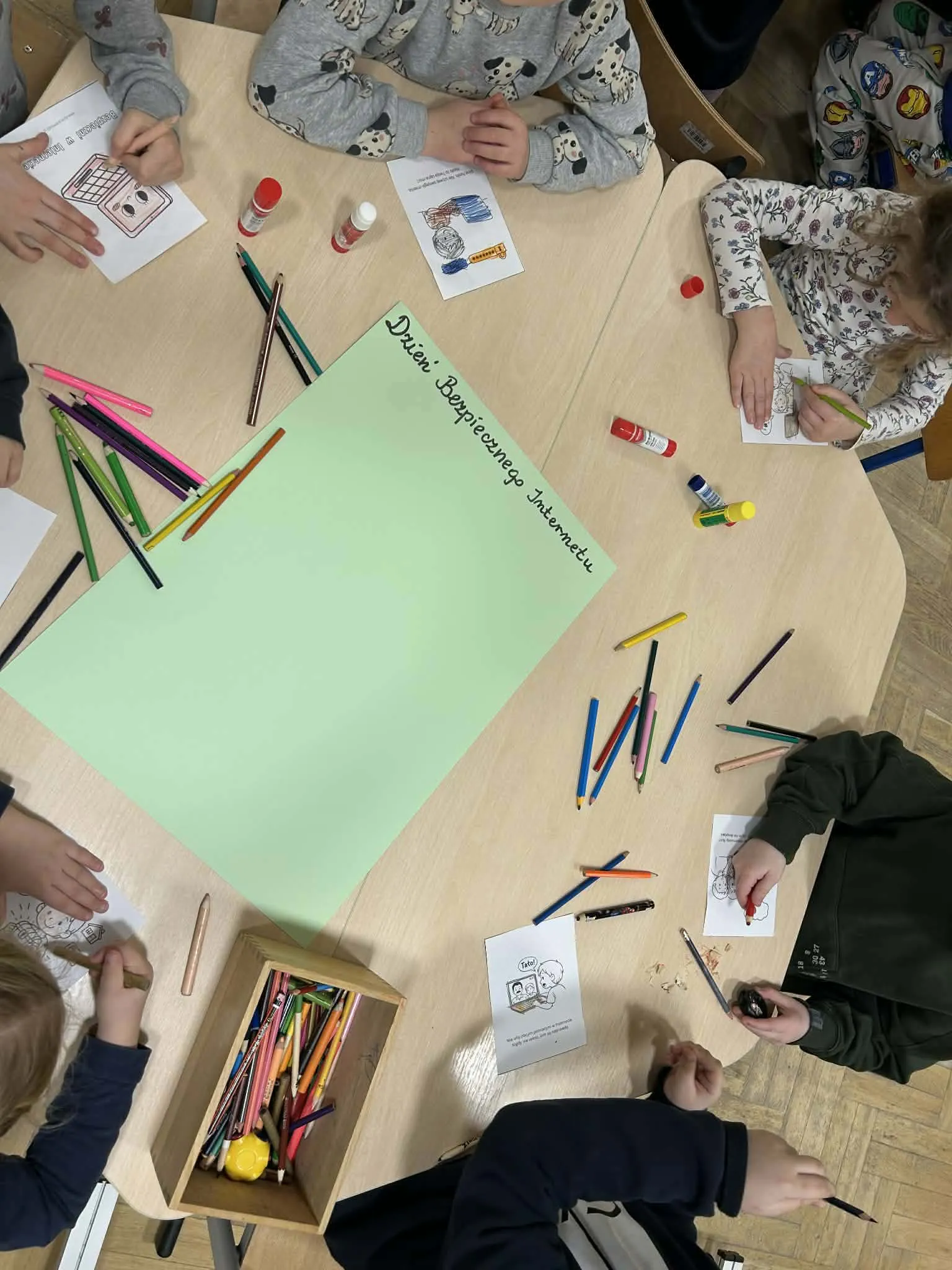 Dzieci siedzą przy stole i kolorują obrazki podczas zajęć z okazji Dnia Bezpiecznego Internetu.