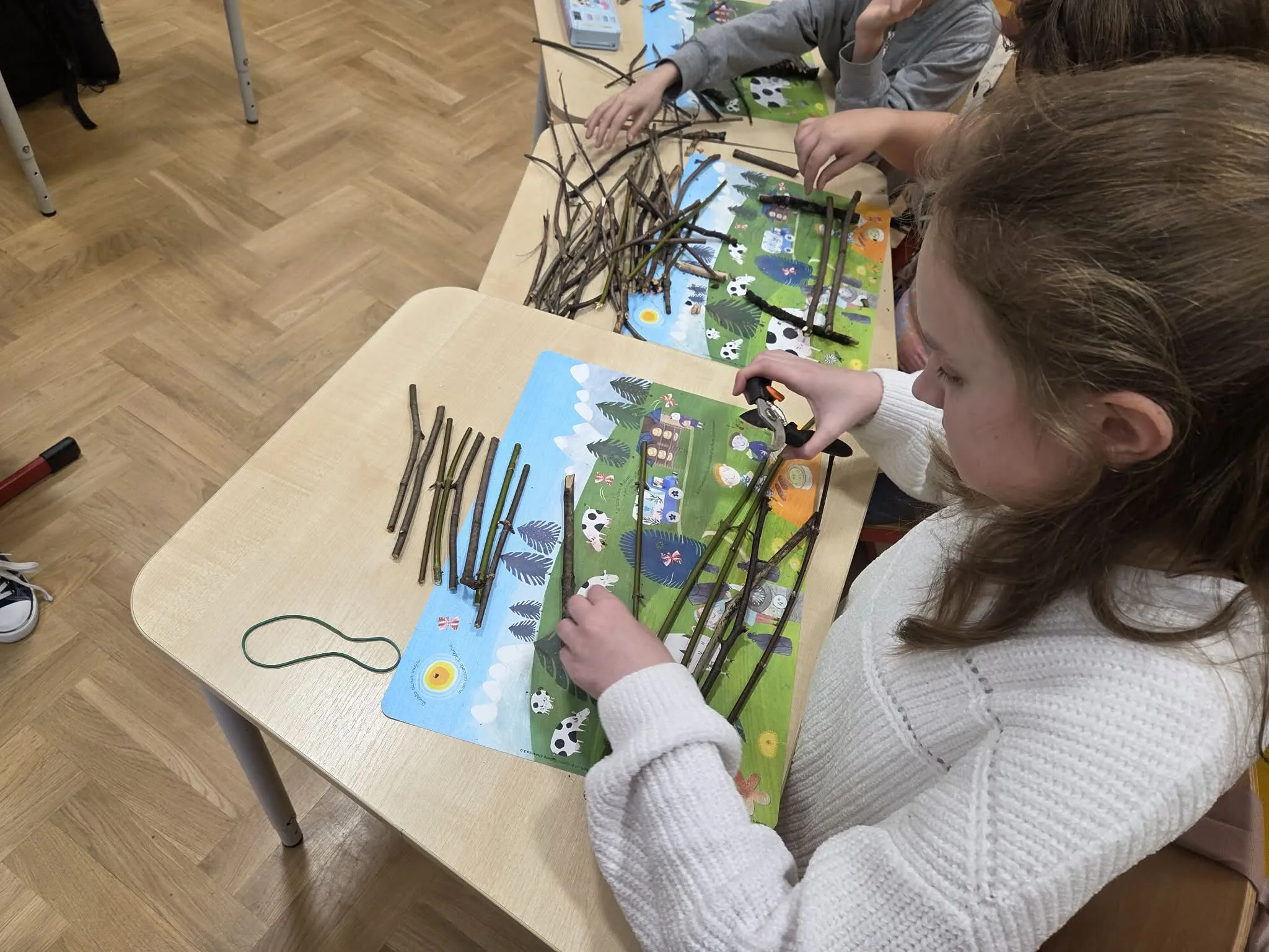 Uczennica tworzy konstrukcję z patyków podczas zajęć plastycznych w klasie