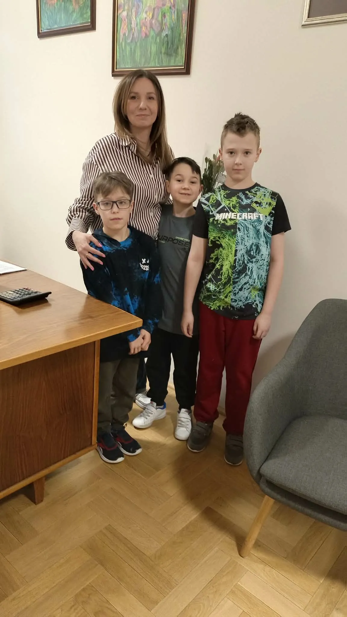 Dyrektorka stoi z trzema uczniami podczas wspólnego zdjęcia w szkolnym gabinecie.