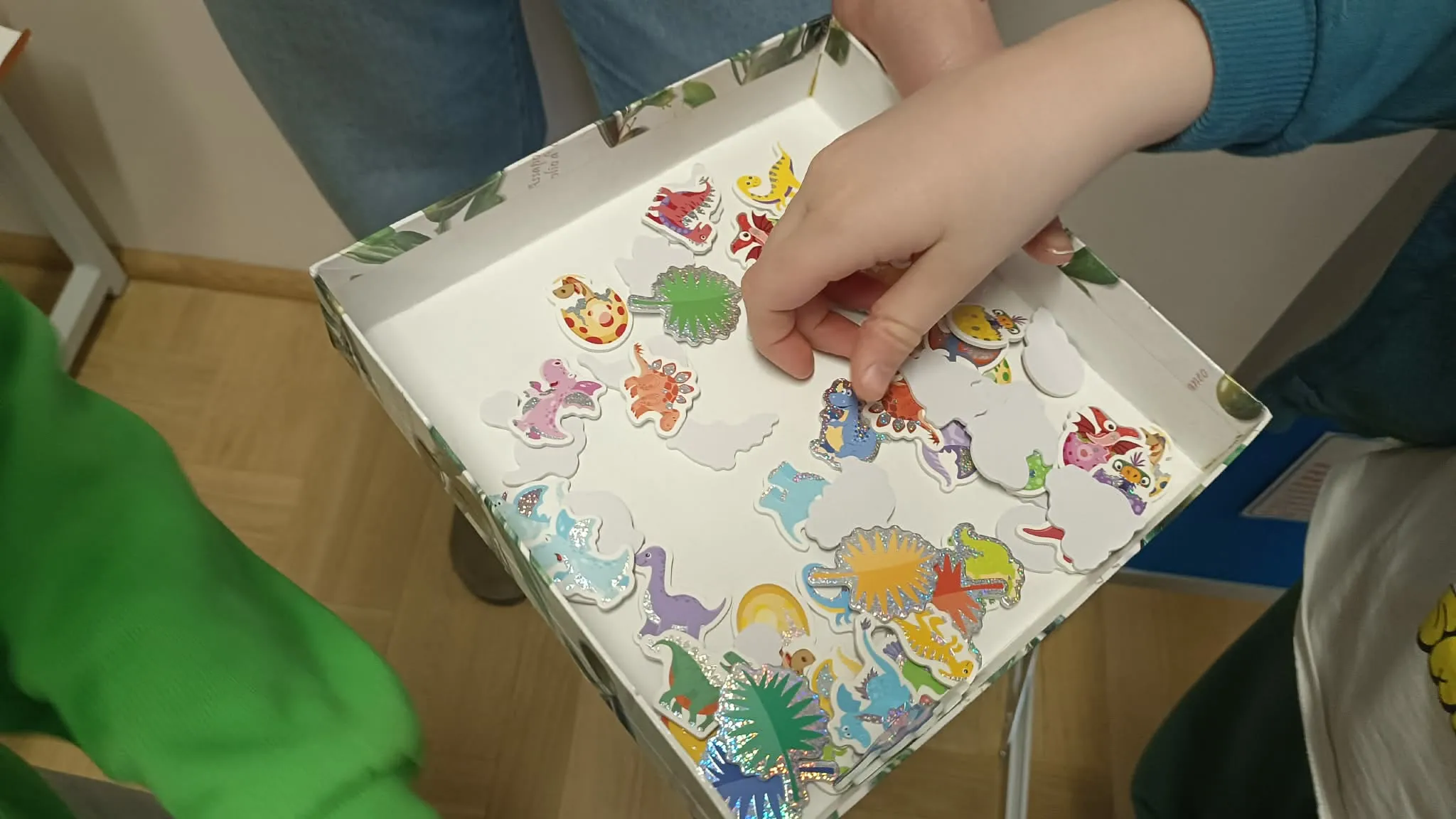 Dziecko wybiera kolorowe naklejki z dinozaurami z pudełka podczas zajęć plastycznych.
