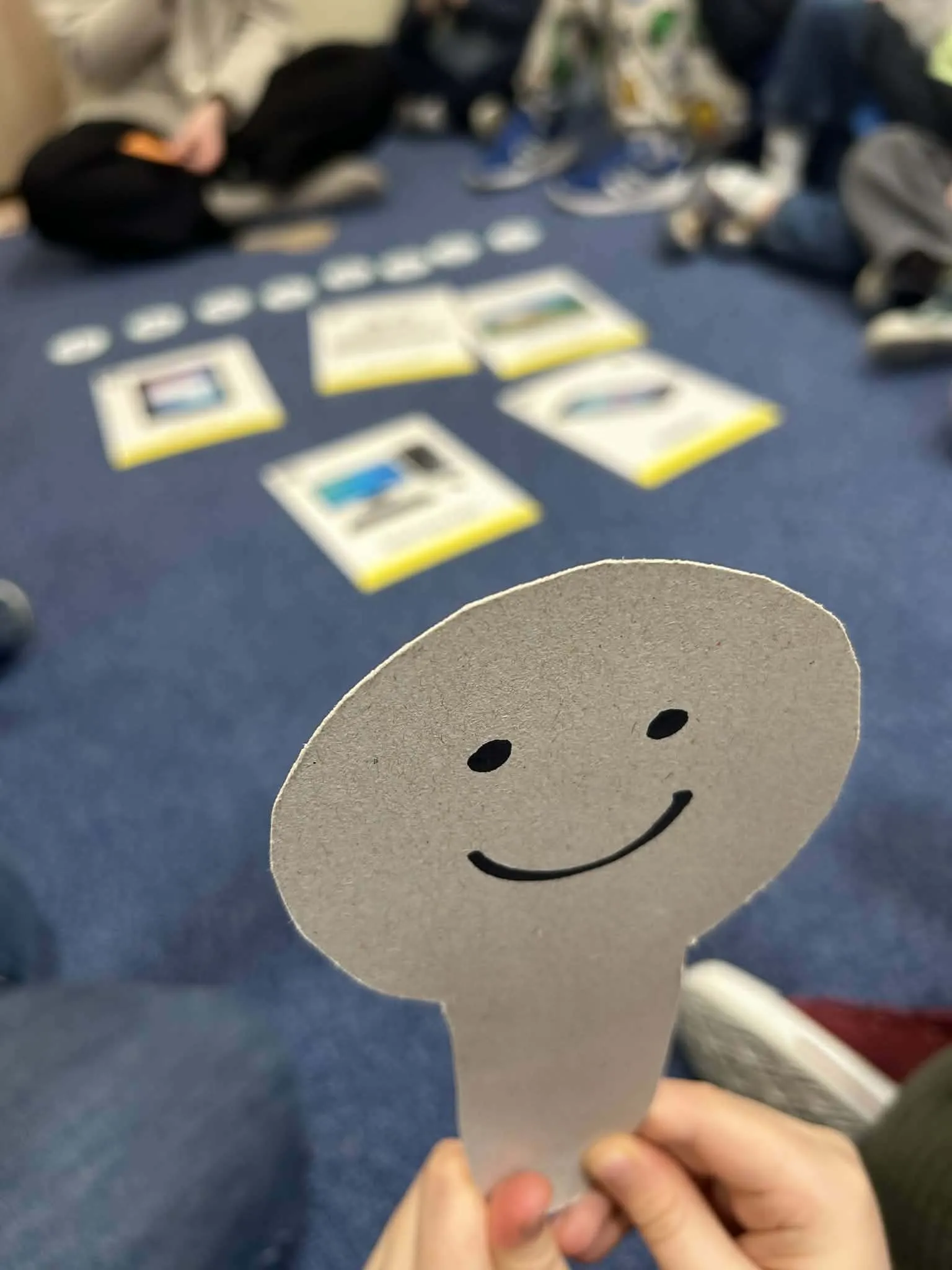 Dziecko trzyma papierową uśmiechniętą buźkę podczas zajęć edukacyjnych o bezpiecznym korzystaniu z internetu.