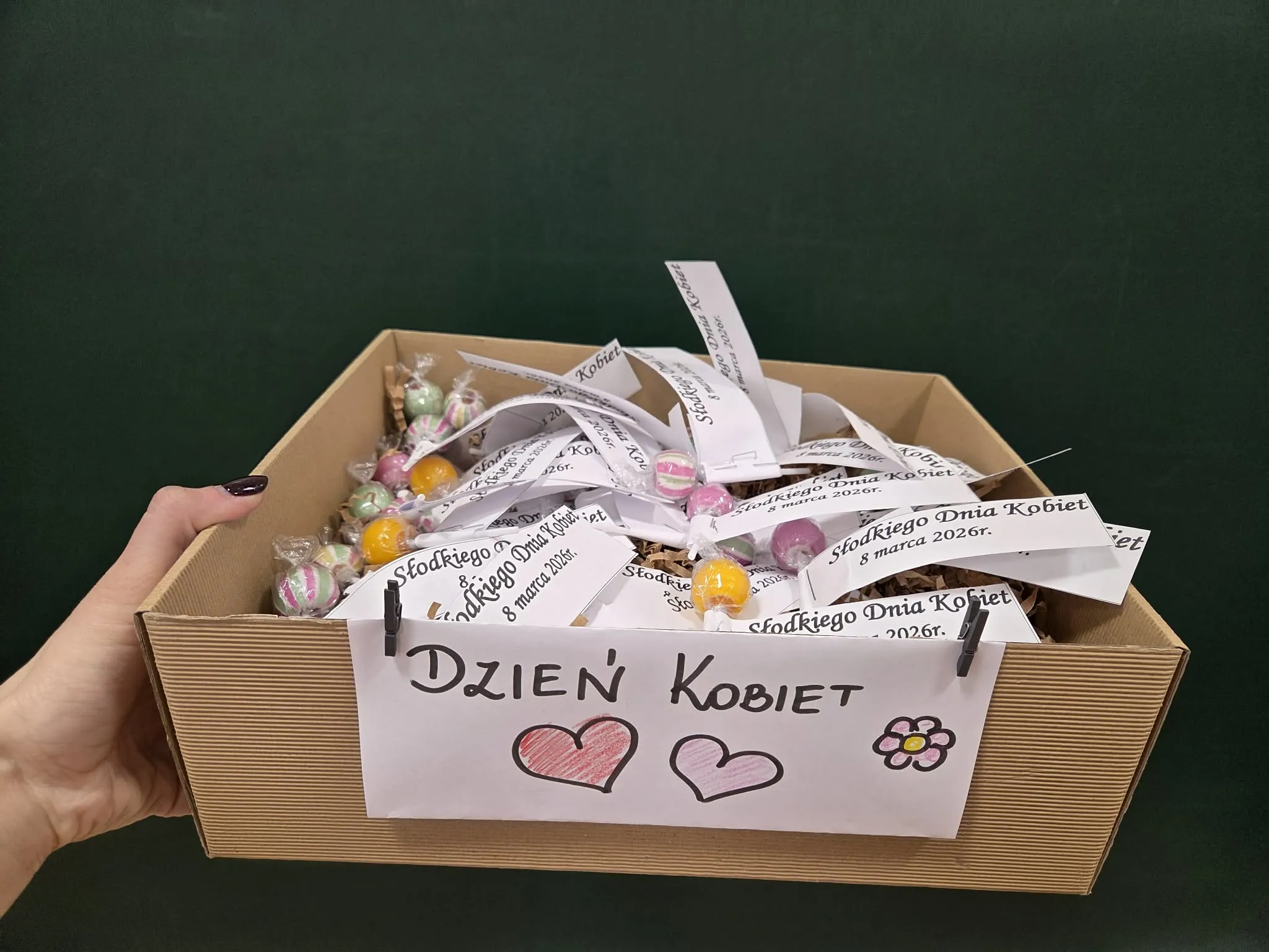 Kartonowe pudełko z cukierkami i karteczkami z życzeniami przygotowane z okazji Dnia Kobiet.