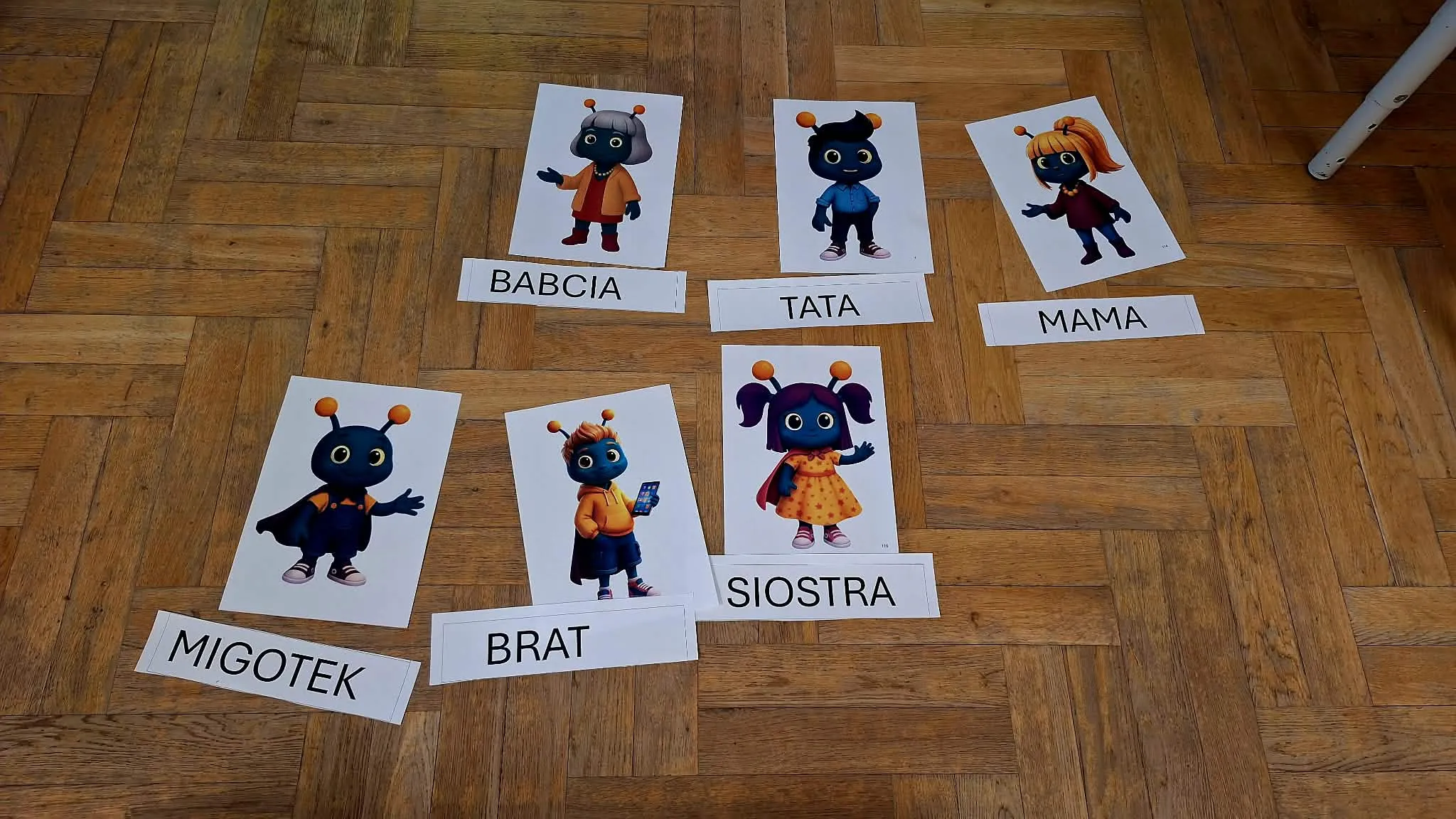 Karty z postaciami i podpisami członków rodziny rozłożone na podłodze.