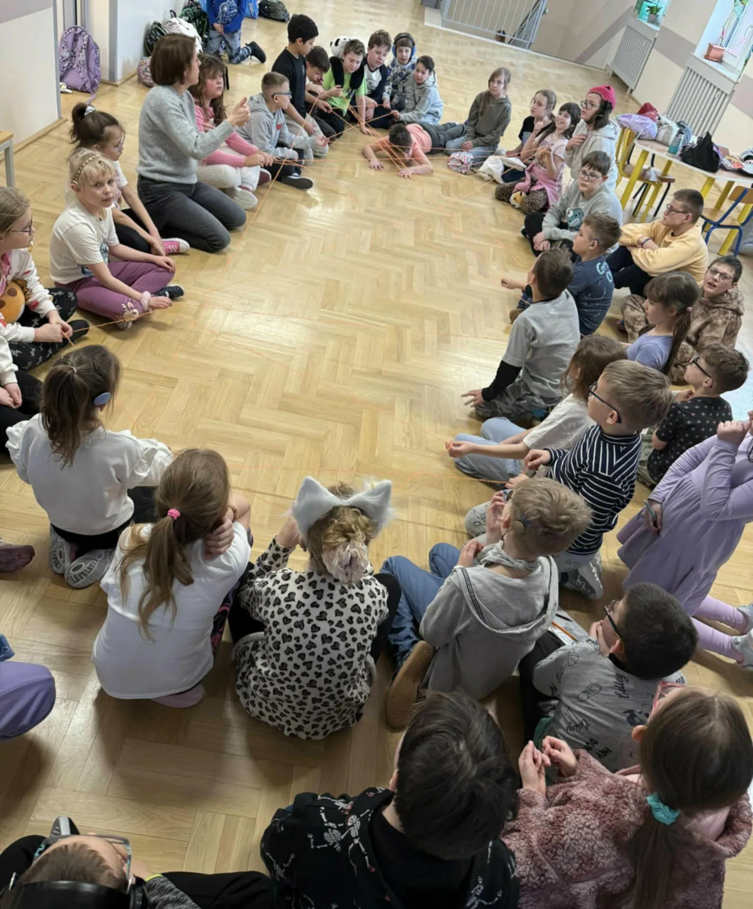 Uczniowie siedzą w dużym kręgu na podłodze i uczestniczą w ćwiczeniu integracyjnym z wykorzystaniem sznurka.