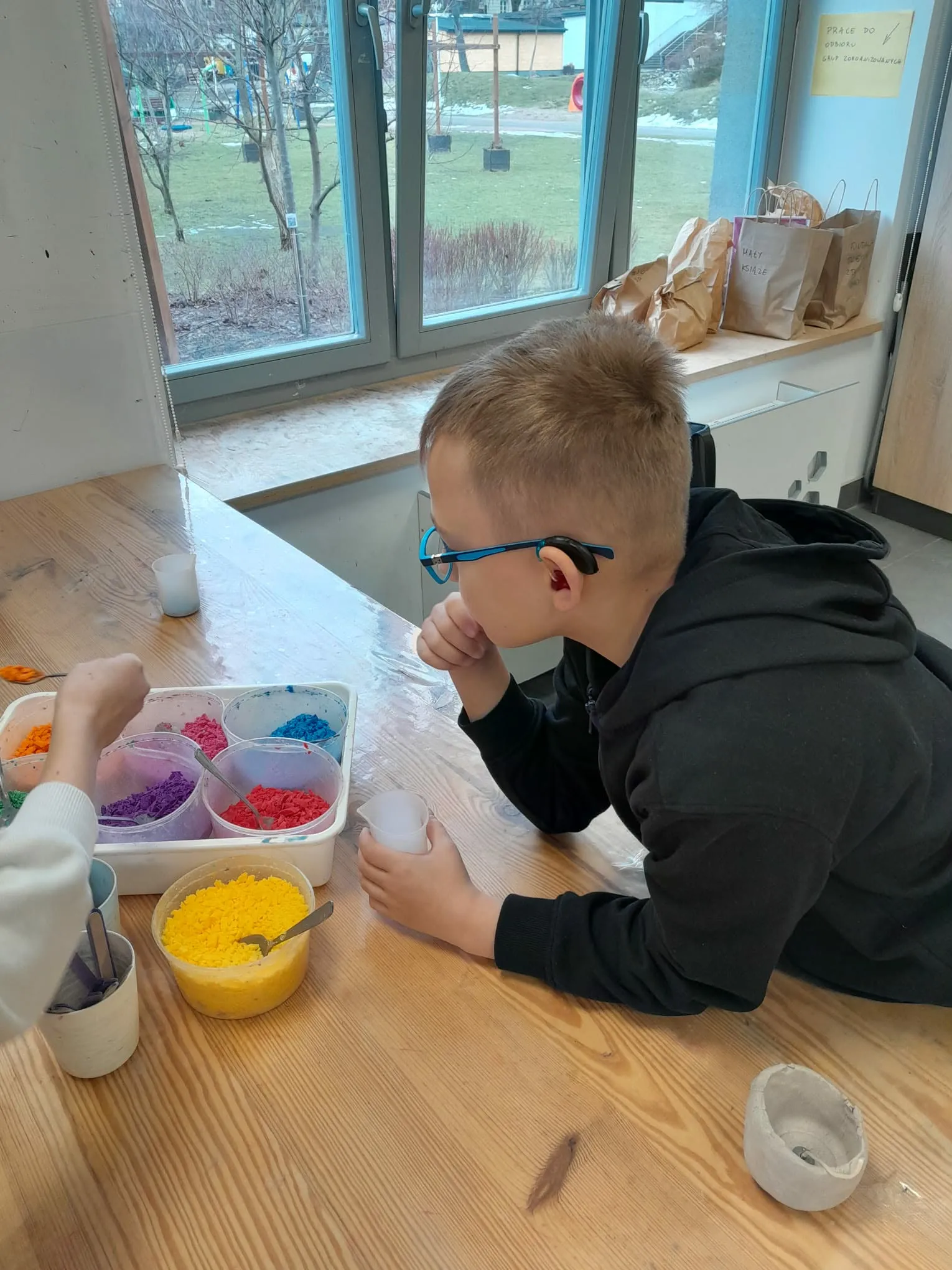 Uczeń przy stole wybiera kolorowy wosk do wykonania własnej świecy podczas zajęć plastycznych.  