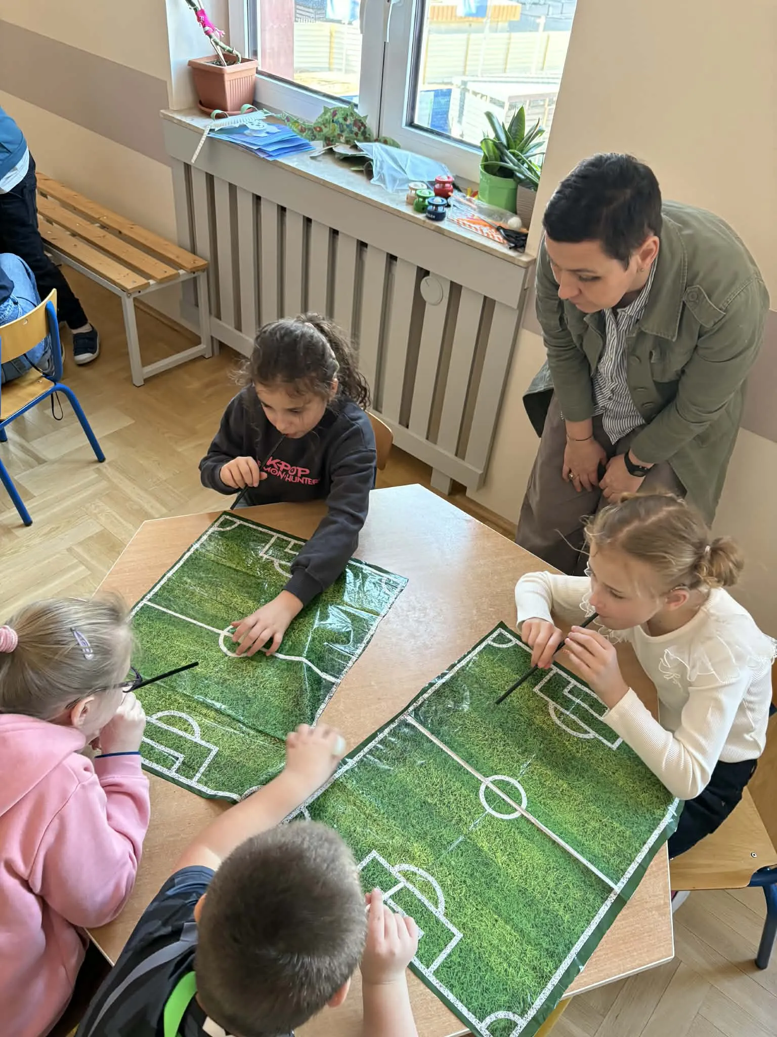 Dzieci dmuchają przez słomki, przesuwając piłeczkę po planszy boiska podczas zabawy