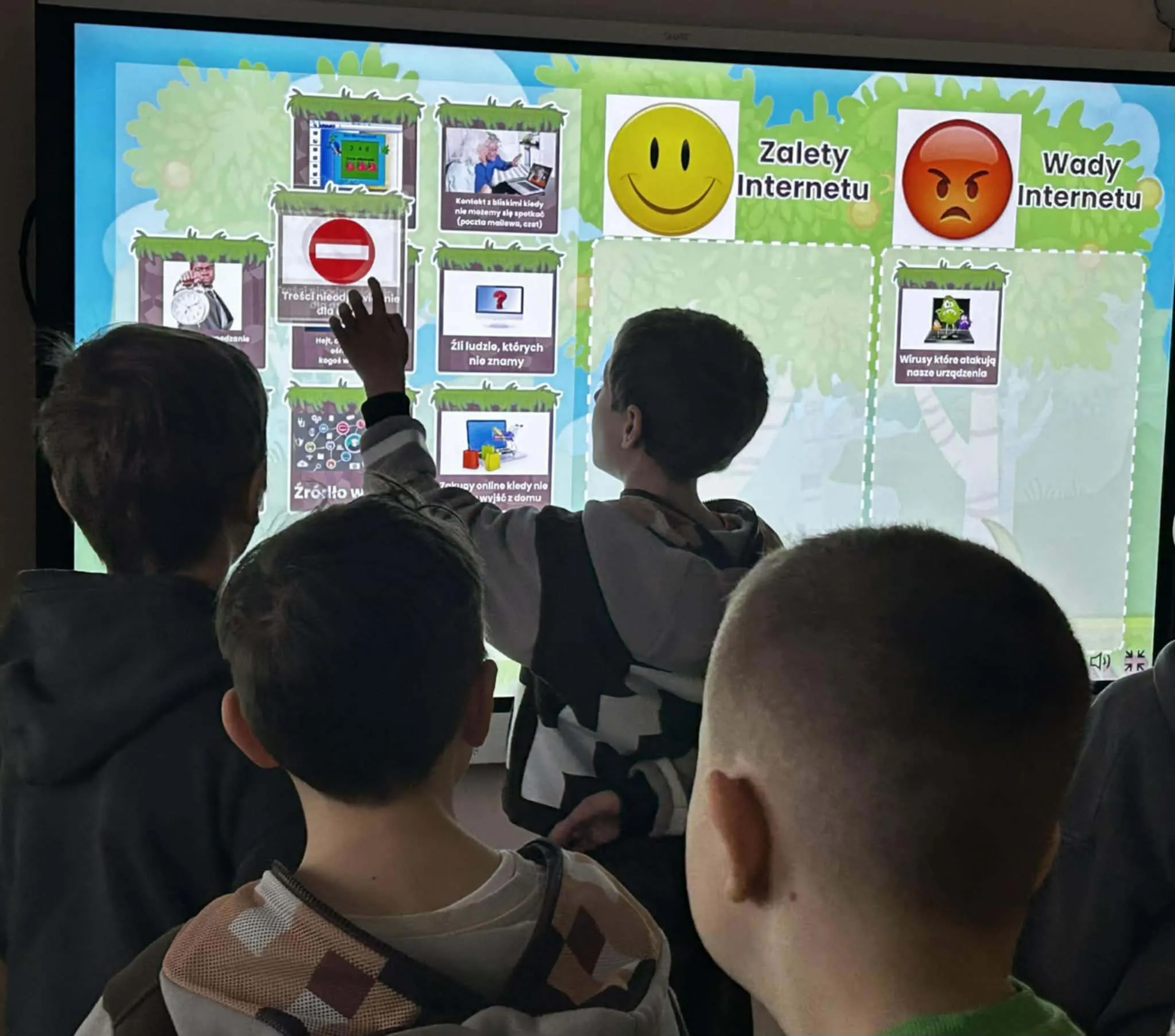 Uczniowie stoją przed tablicą interaktywną i wybierają przykłady zalet oraz wad korzystania z internetu.
