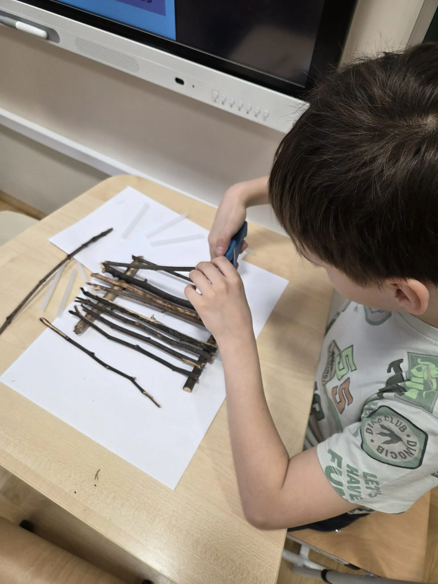 Chłopiec skleja patyki na kartce tworząc model tratwy