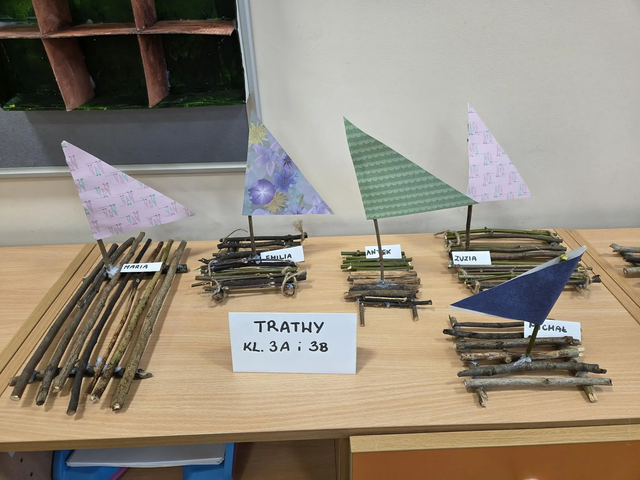 Modele tratw z patyków wykonane przez uczniów i podpisane imionami