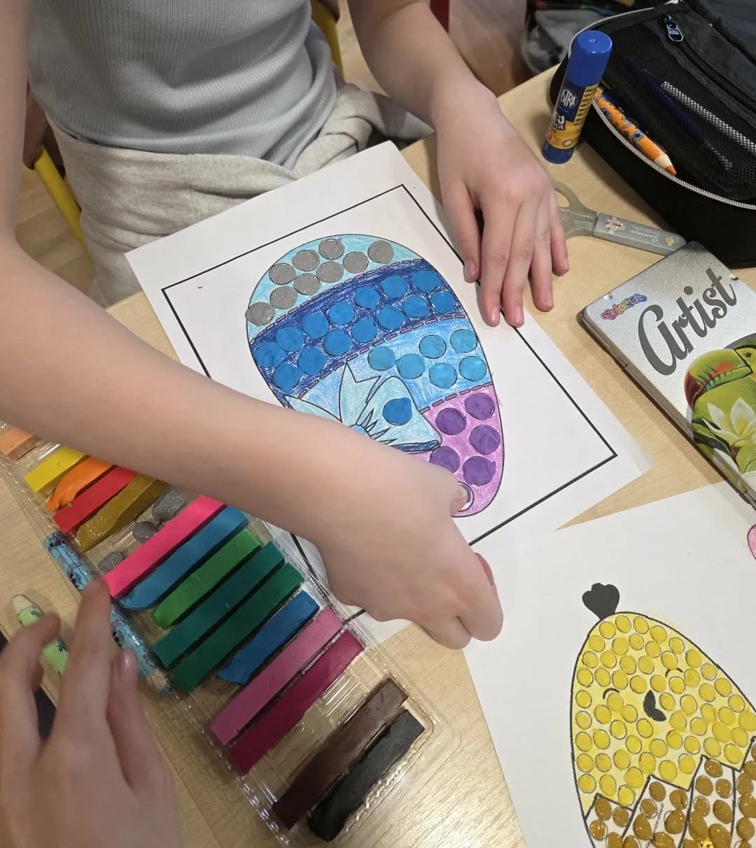 Uczennica ozdabia papierowe jajko kolorową plasteliną podczas zajęć plastycznych