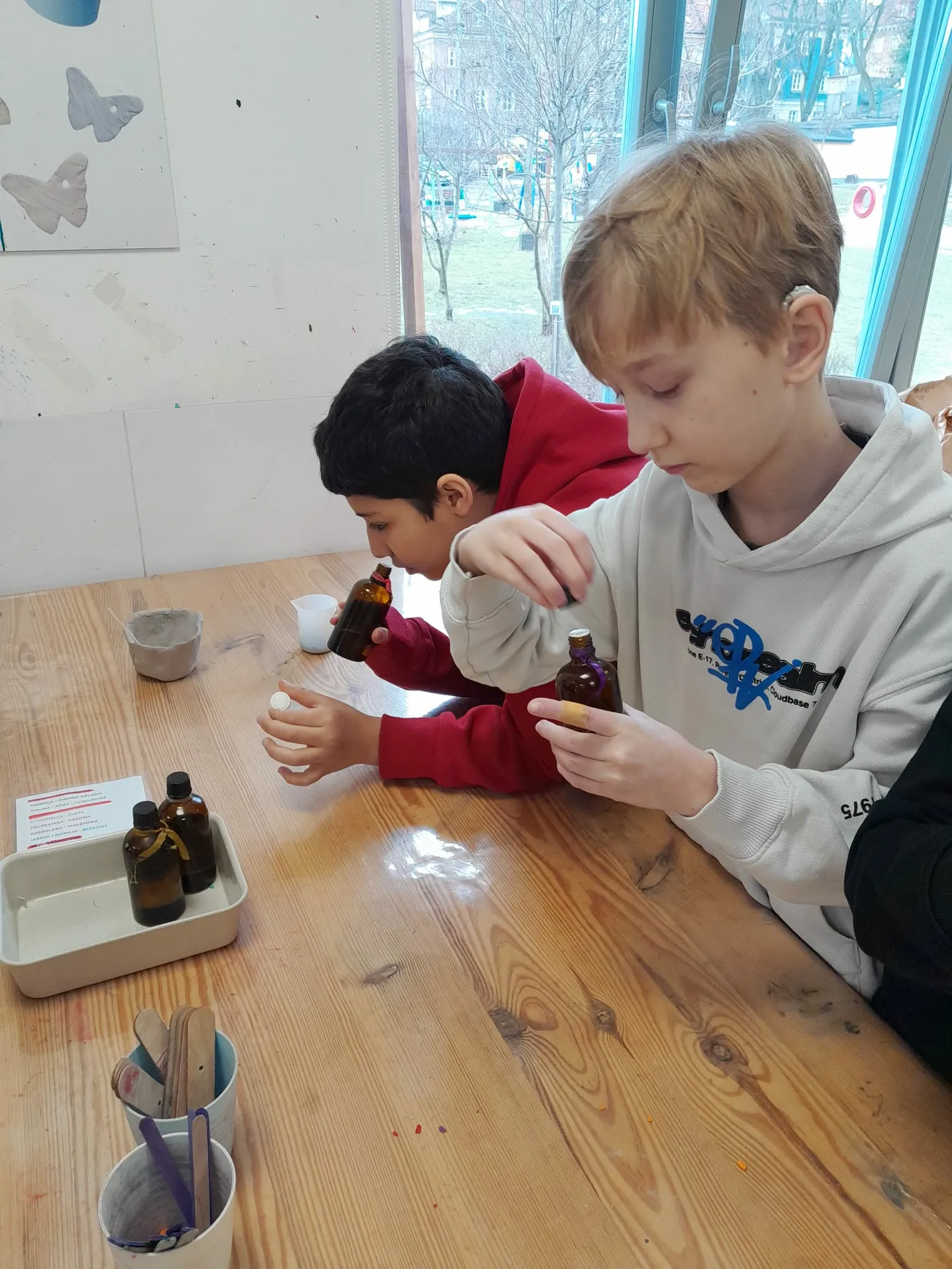 Dwóch uczniów odmierza olejki zapachowe z butelek podczas warsztatów tworzenia świec.