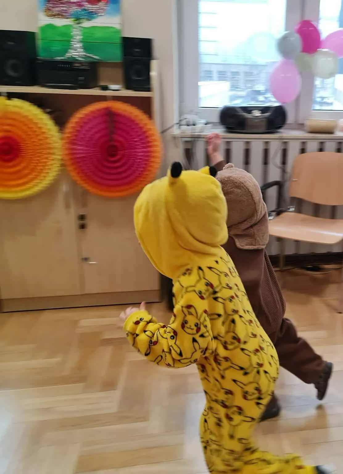 Dwoje dzieci w kostiumach biegnie po sali podczas zabawy karnawałowej.