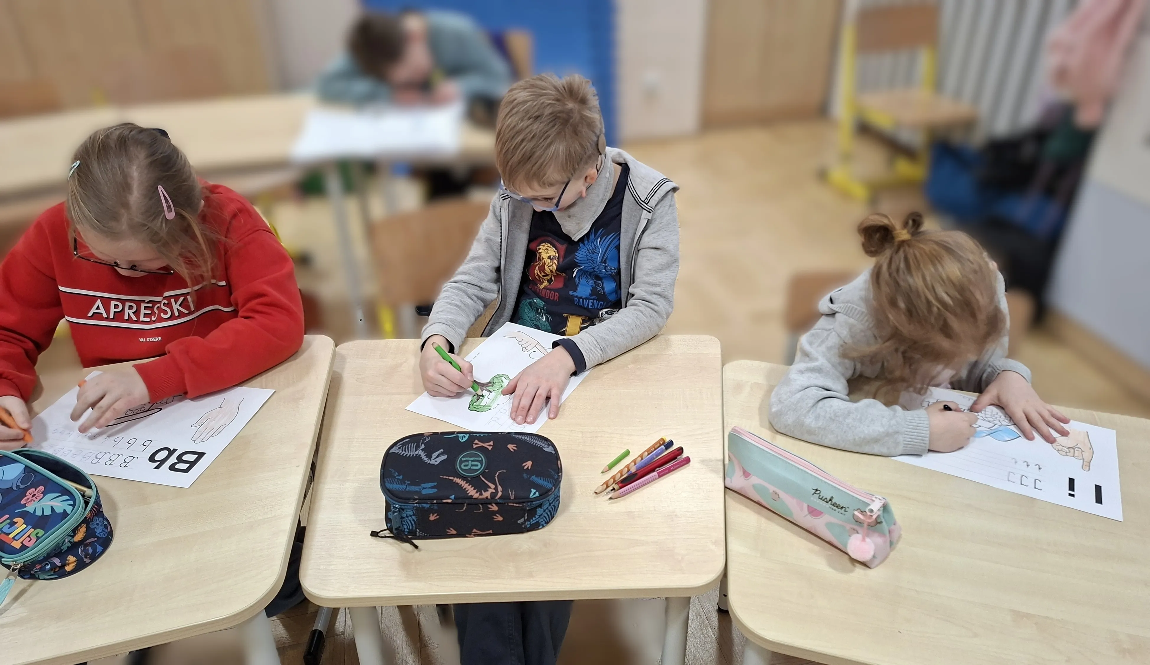 Dzieci siedzą przy ławkach i kolorują obrazki kredkami