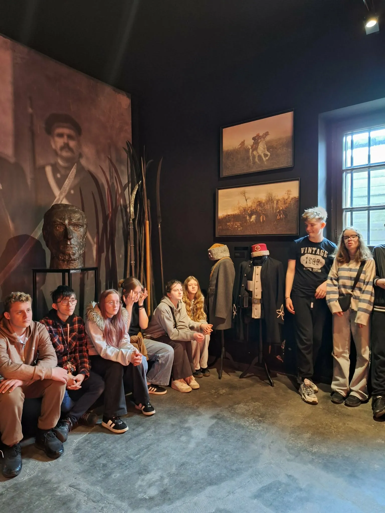 Uczniowie słuchają przewodnika w sali muzealnej z eksponatami historycznymi