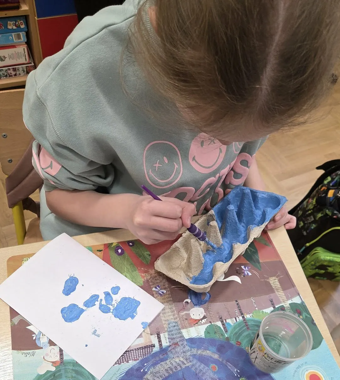 Dziecko maluje farbą wytłoczkę po jajkach podczas zajęć plastycznych