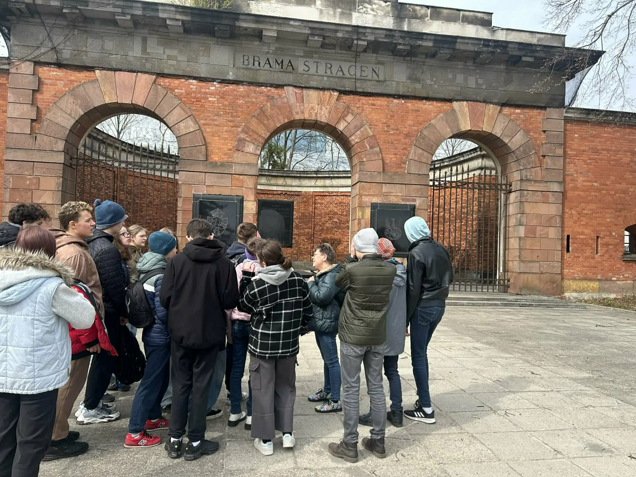 Grupa uczniów stoi przed zabytkową Bramą Straceń podczas wycieczki edukacyjnej