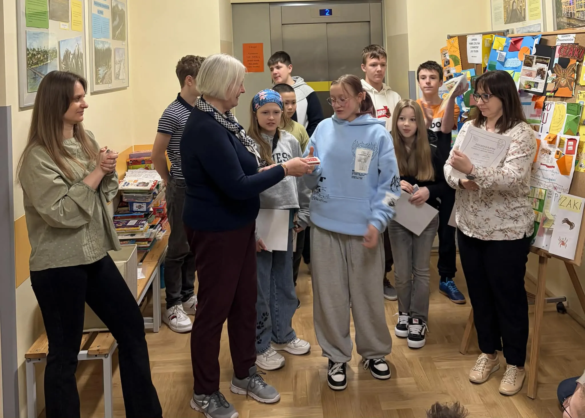 Nauczycielka wręcza uczennicy nagrodę w obecności grupy uczniów