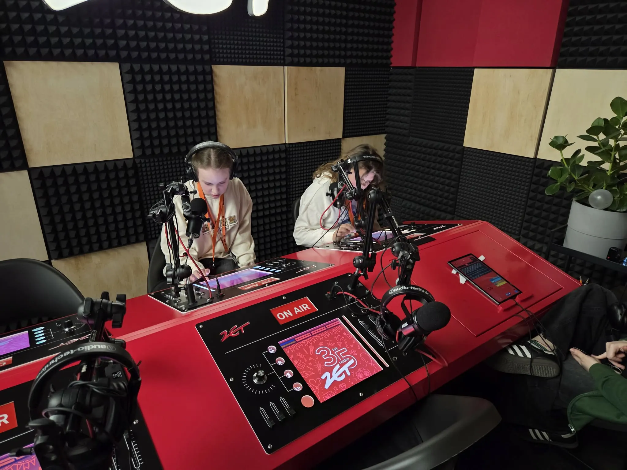 Uczniowie podczas zajęć w studiu radiowym siedzą przy mikrofonach i konsoli nagraniowej