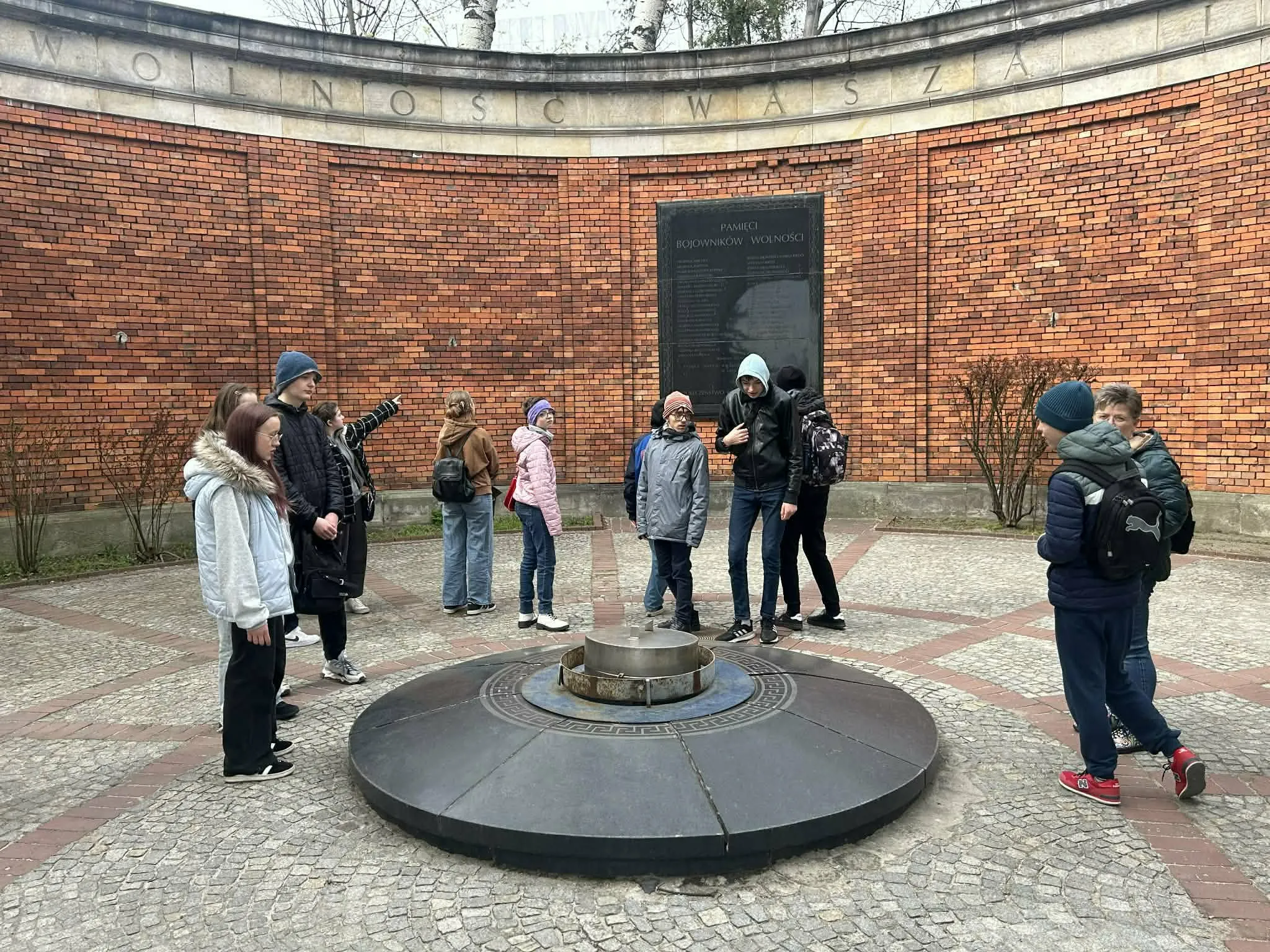 Grupa uczniów stoi wokół symbolicznego miejsca pamięci na muzealnym dziedzińcu