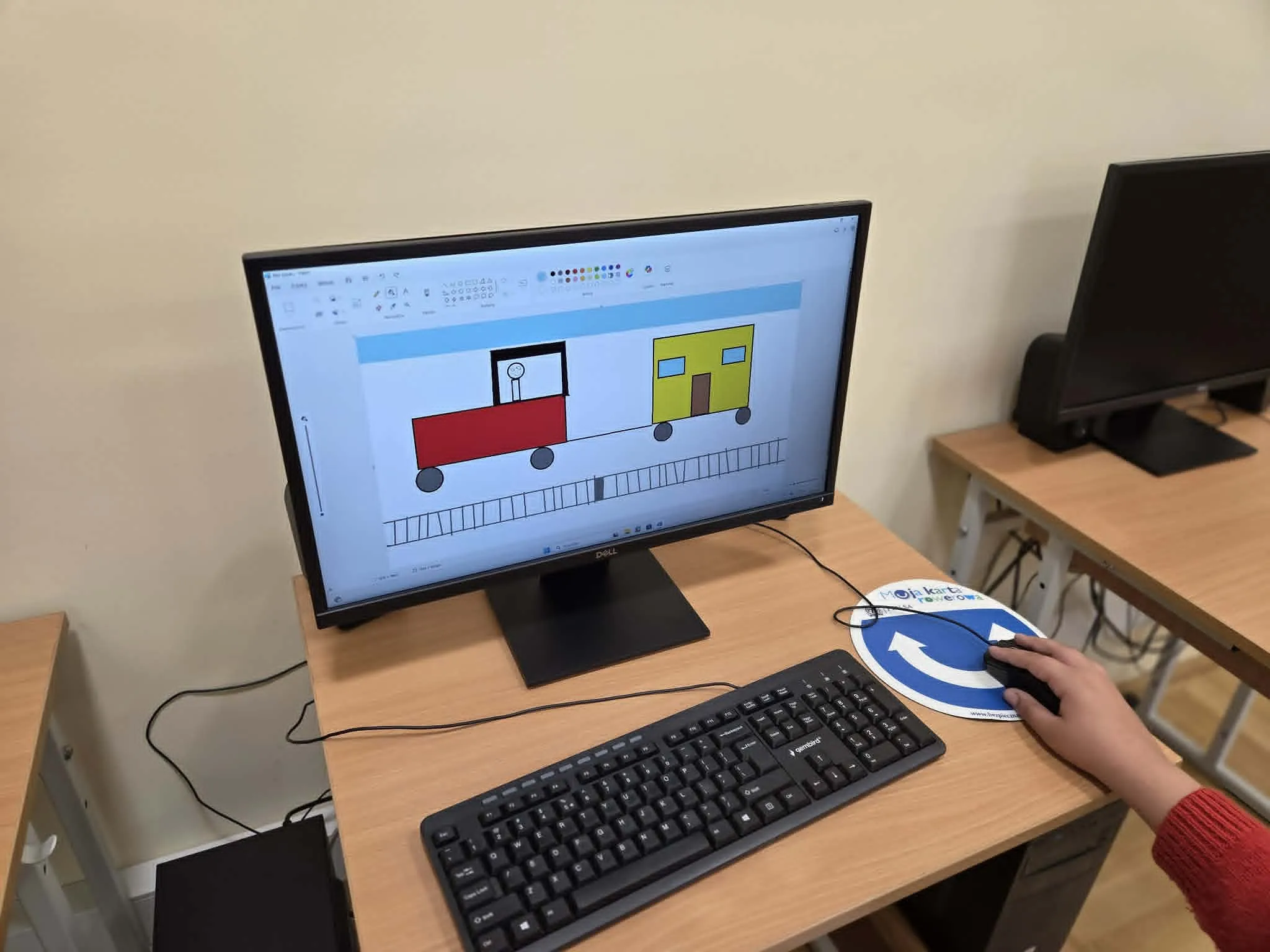 Uczeń siedzi przy komputerze i tworzy w programie Paint kolorowy rysunek pociągu na torach.