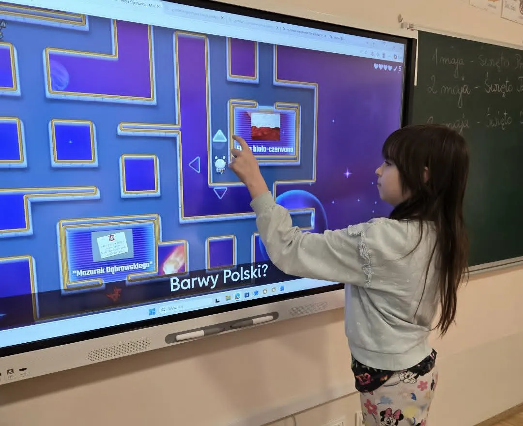 Dziewczynka rozwiązuje interaktywny quiz o barwach Polski na dużej tablicy multimedialnej w sali lekcyjnej. 