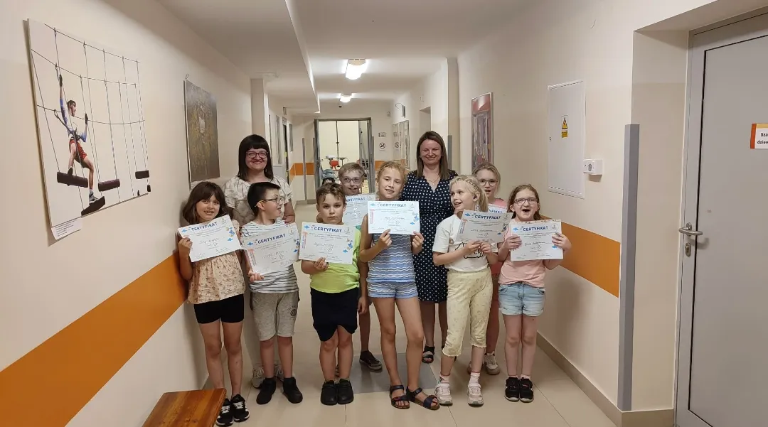 Grupa uczniów wraz z nauczycielkami prezentuje certyfikaty otrzymane za udział w Ogólnopolskim Projekcie Edukacyjnym „Ogólnorozwojowy Język Migowy”.